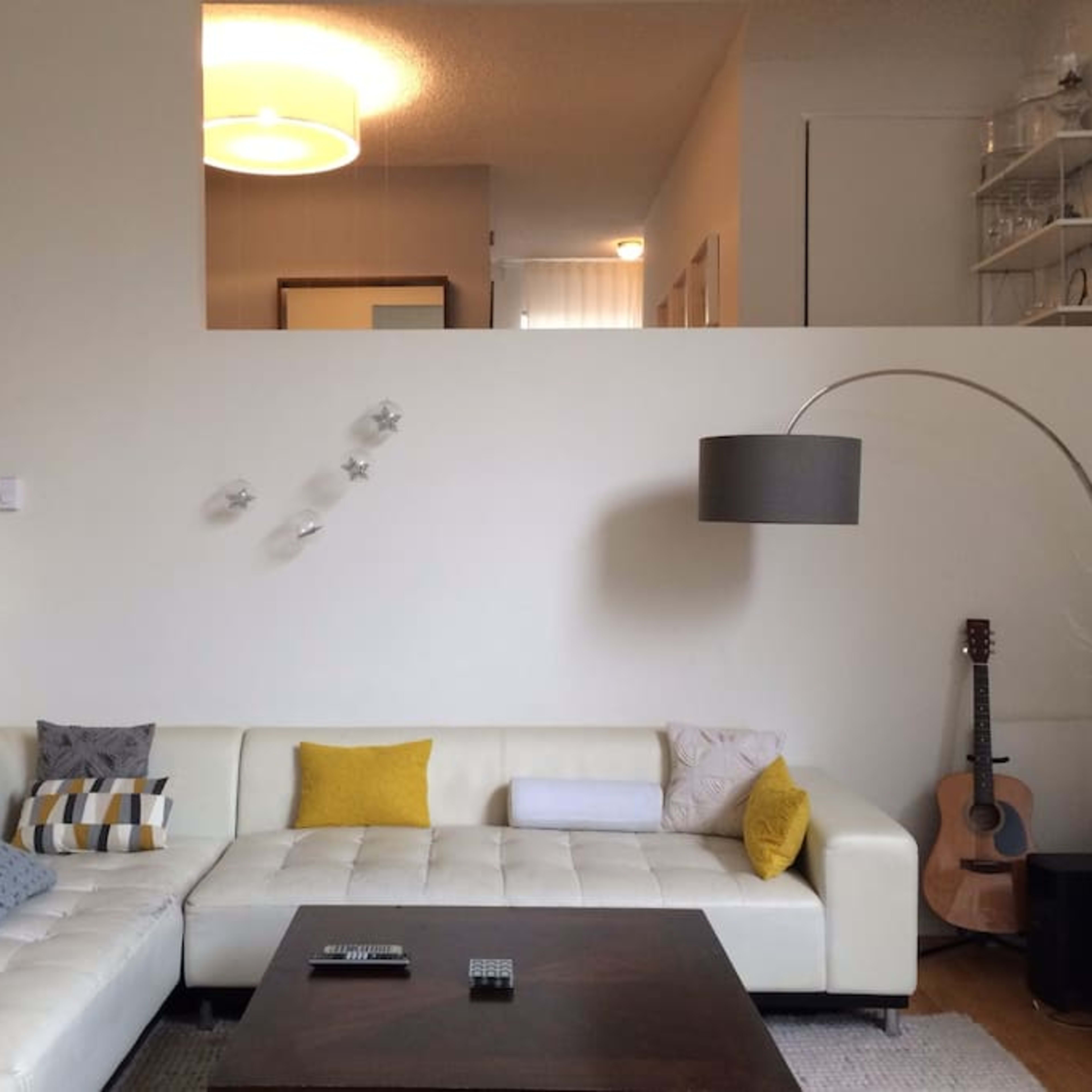 A modern living room features a white sectional sofa with colorful cushions, a wooden coffee table, and a guitar in the corner, with a staircase visible in the background.