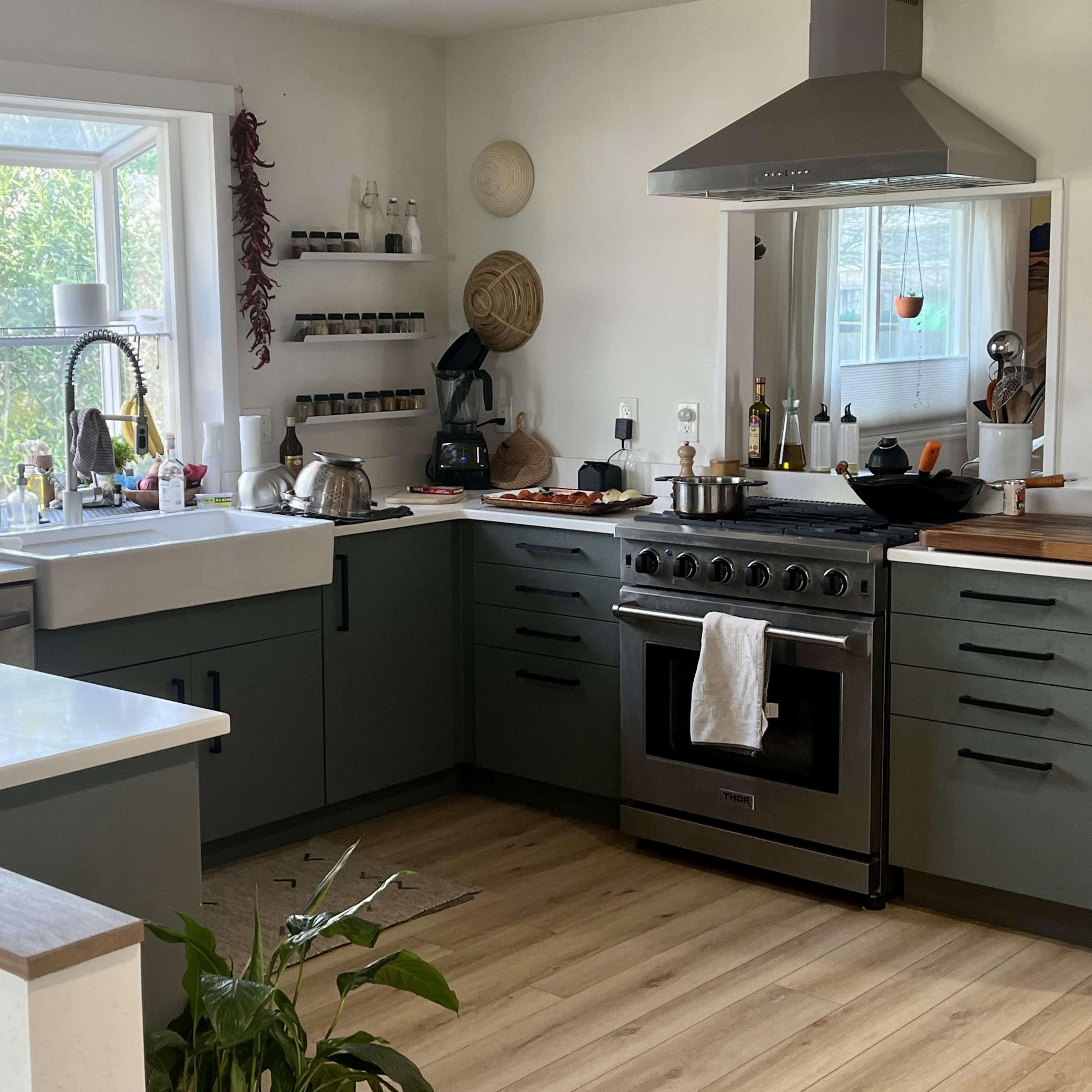 A modern kitchen features a spacious island with a sink, a range hood above a stove, and large windows providing natural light.