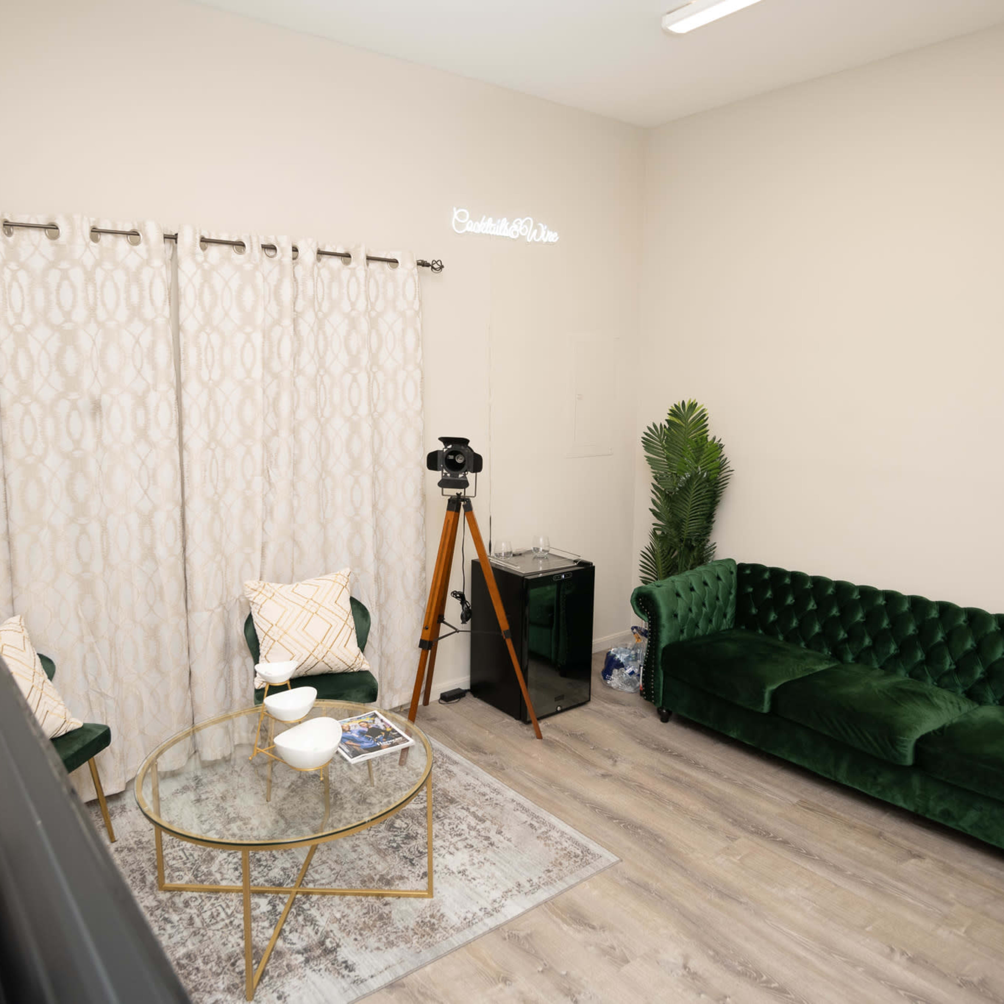 A cozy room with a green velvet sofa, a glass coffee table, a decorative curtain, and a vintage camera on a tripod.