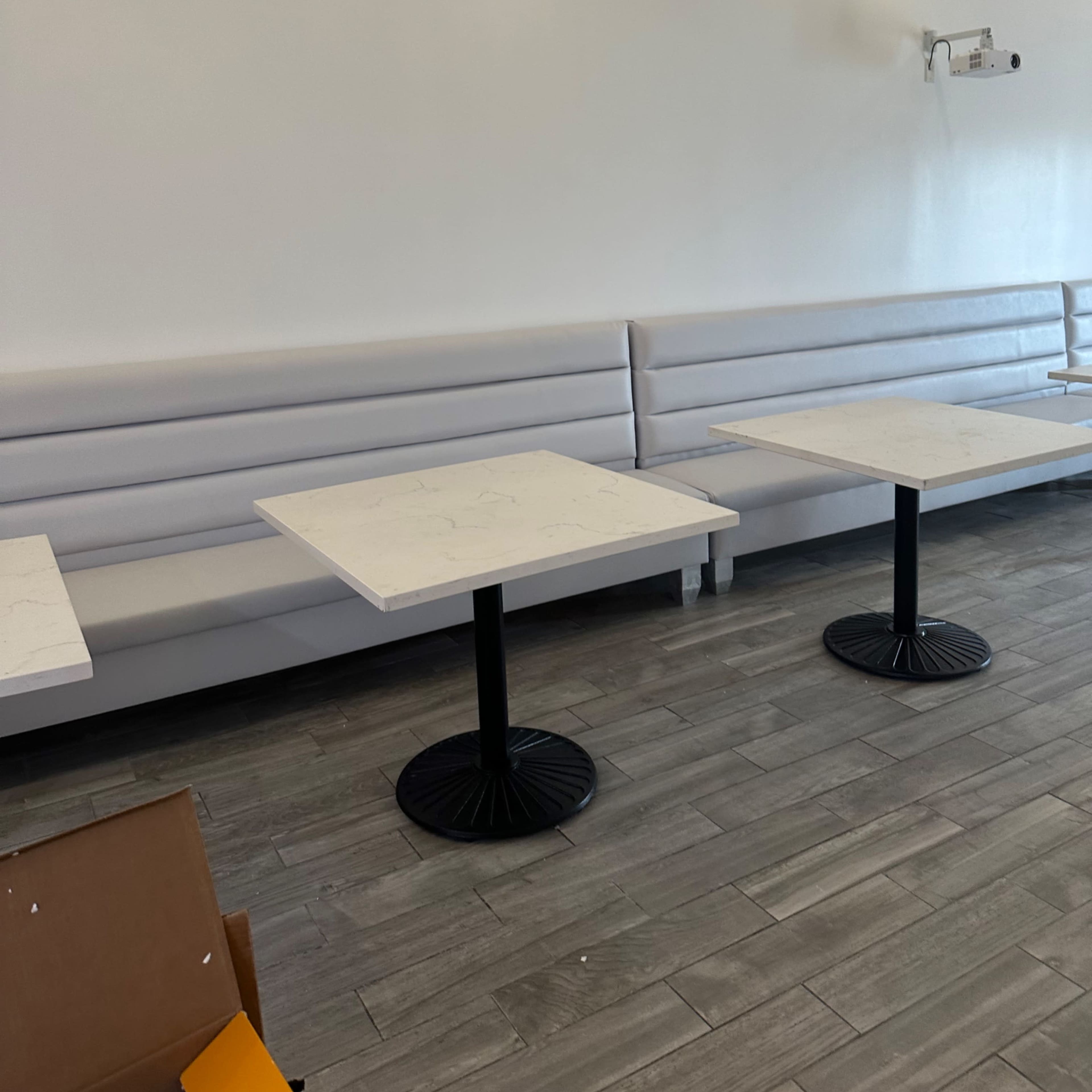 A sparsely furnished restaurant interior with white walls, marble-topped tables, and gray seating along one side.