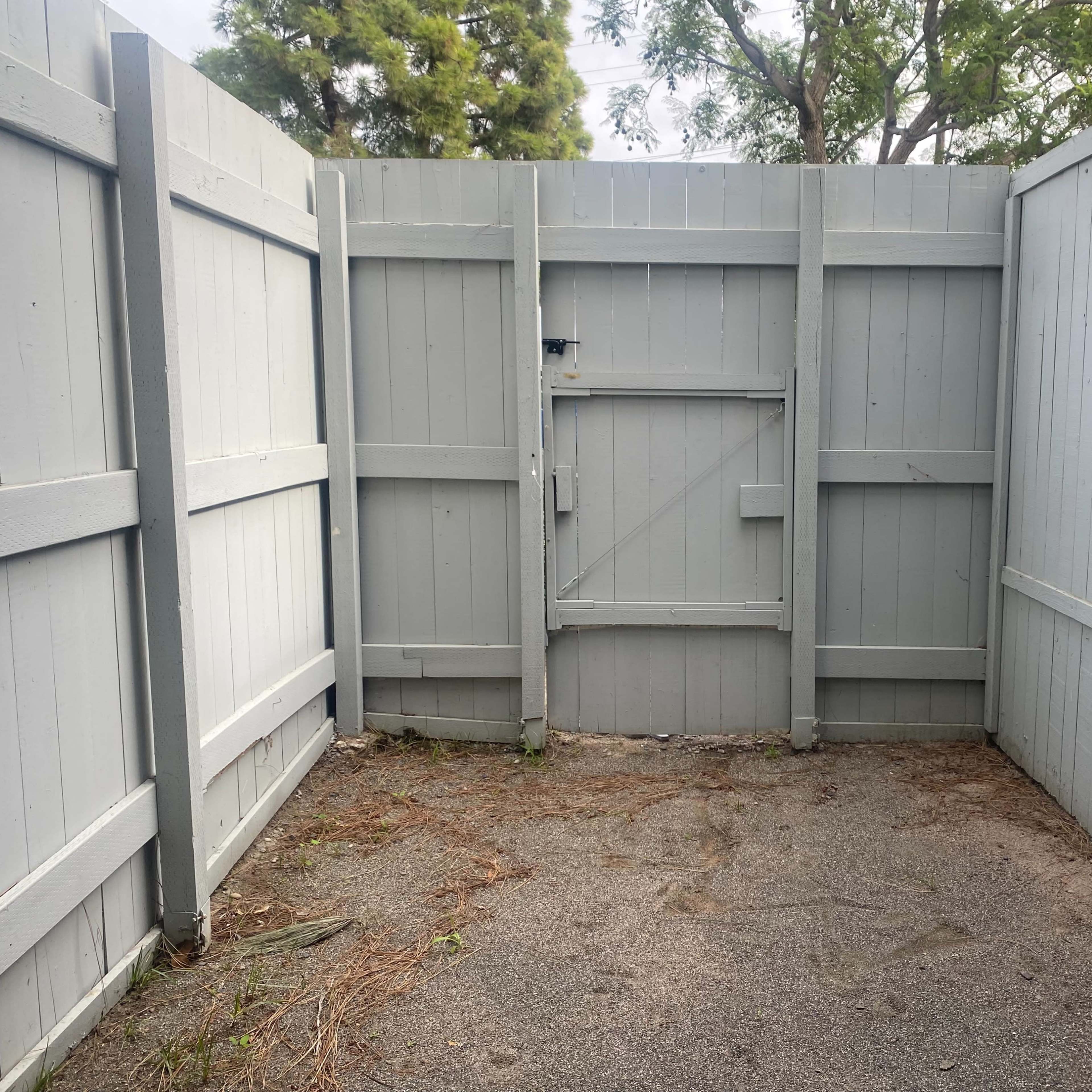 A small, enclosed outdoor area with light gray wooden fences and a single gate.