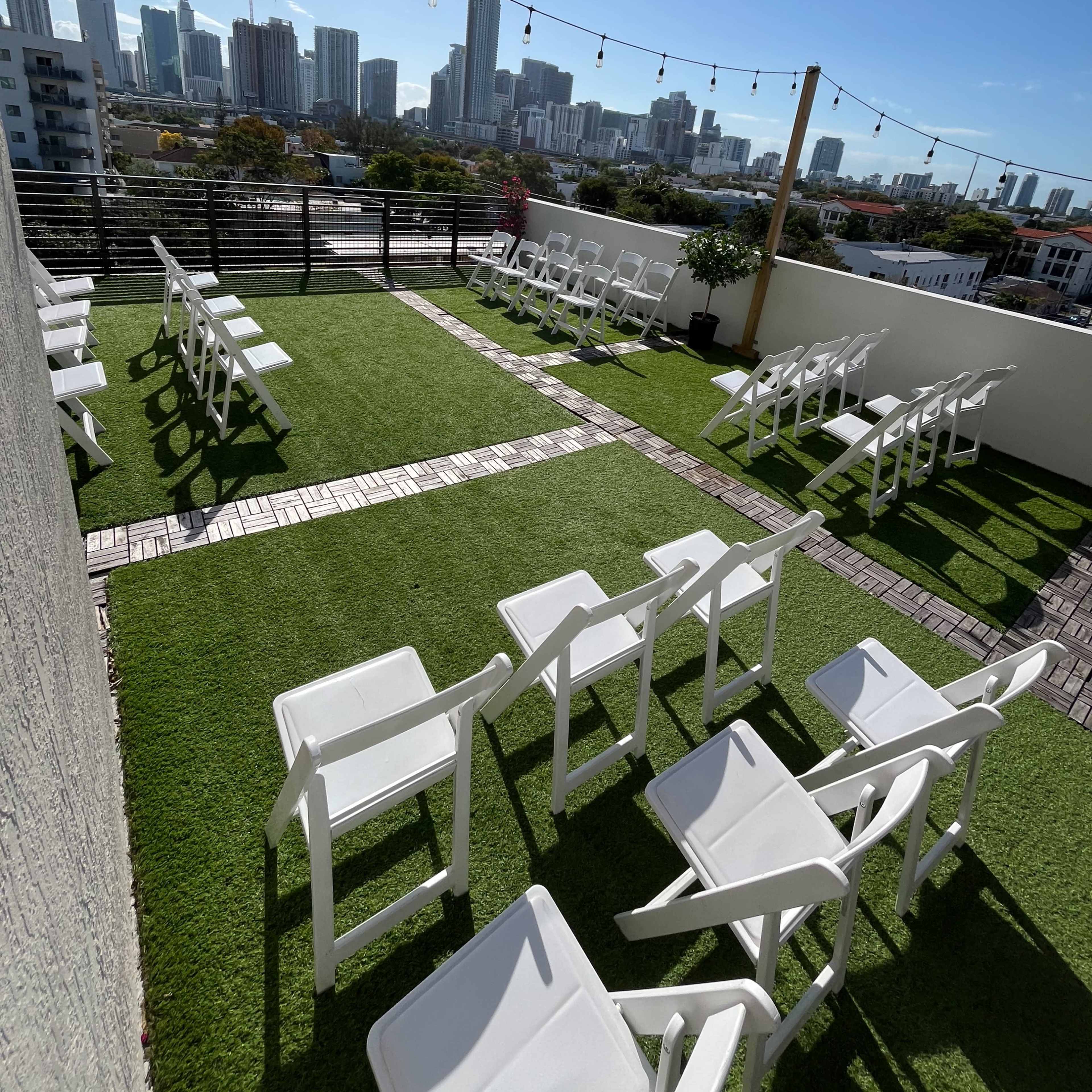 A rooftop venue with white chairs arranged neatly on artificial grass, overlooking a city skyline.