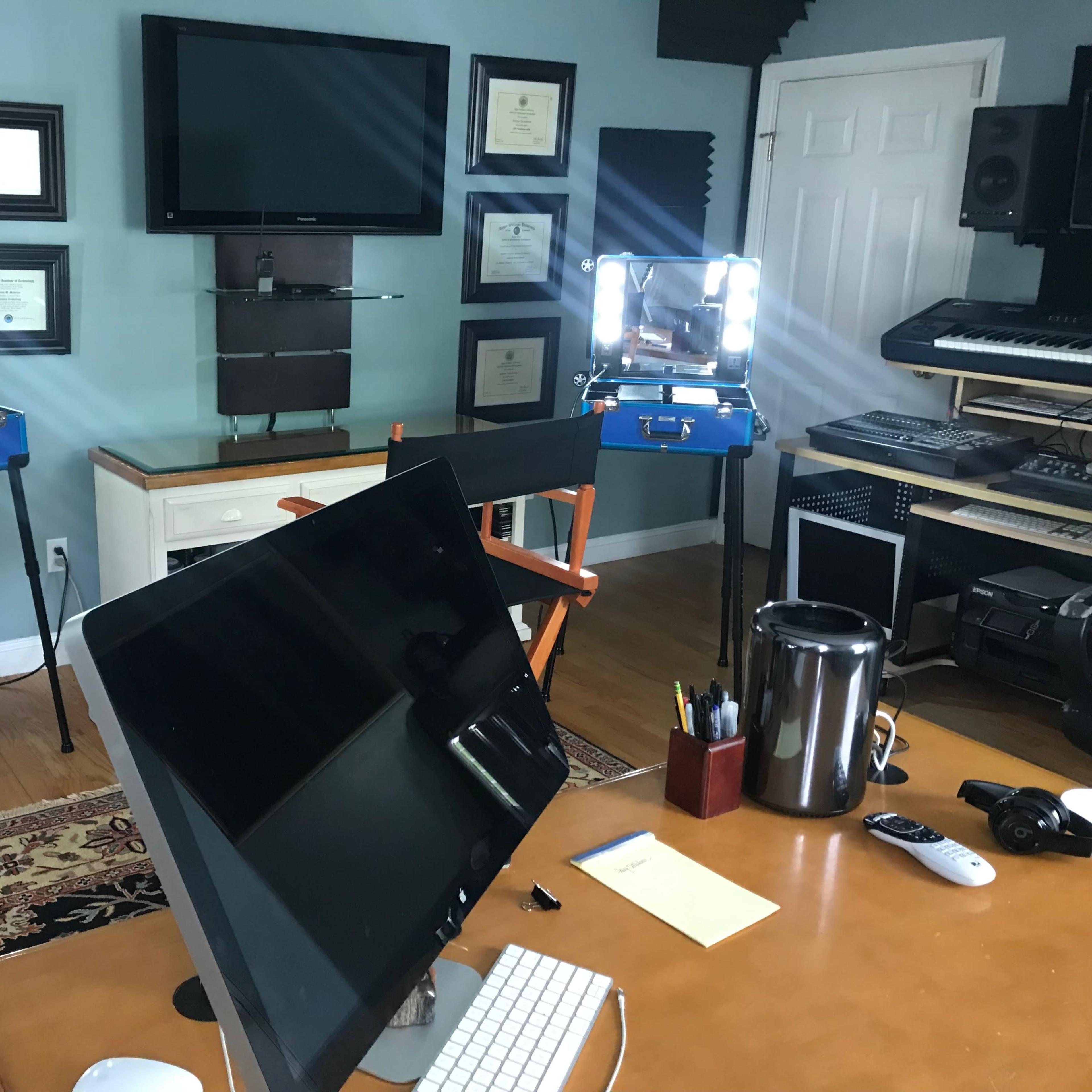 A room with a large monitor, two illuminated makeup stations, a desk, and various musical equipment.