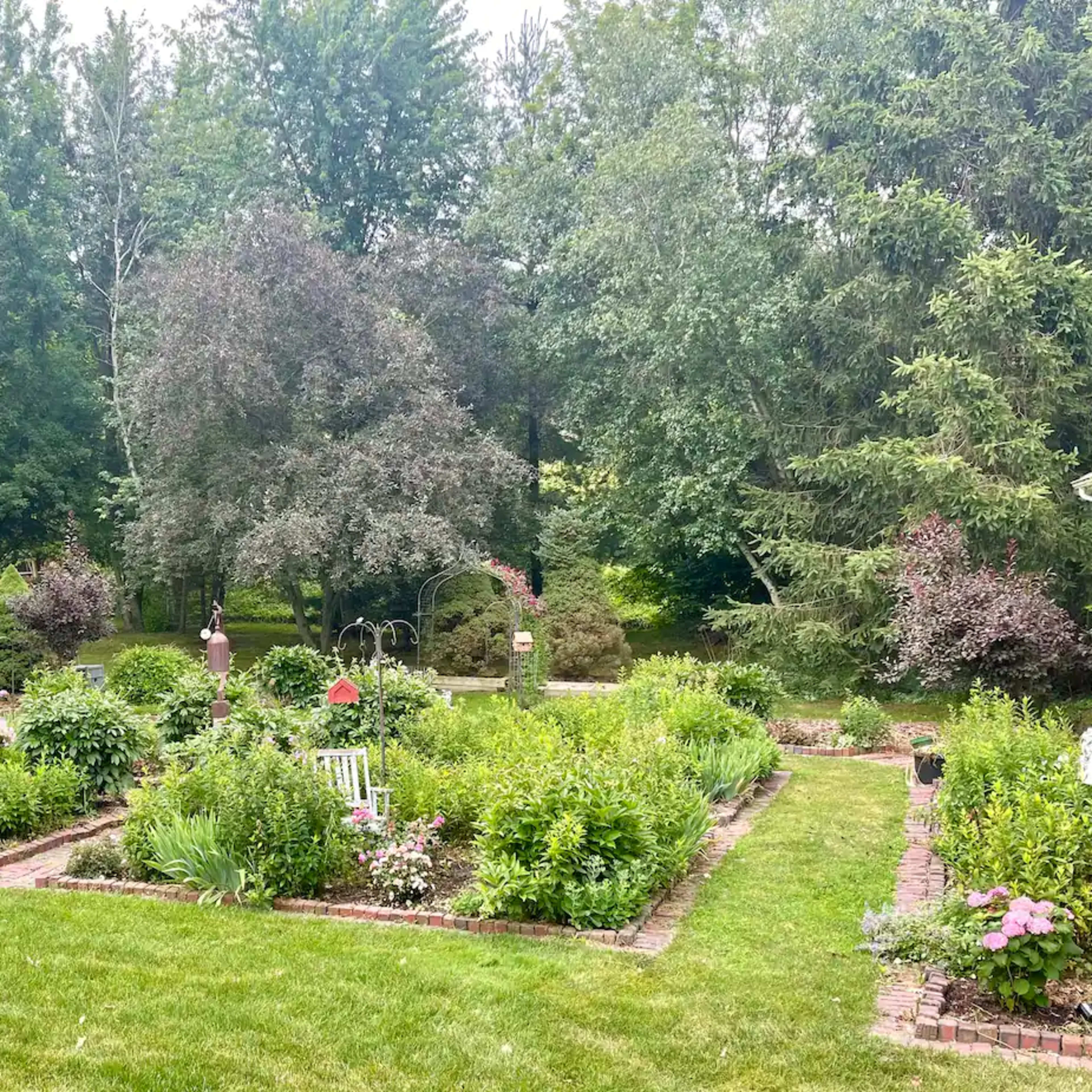 A landscaped garden with neatly arranged flower beds, pathways, and greenery surrounded by trees.