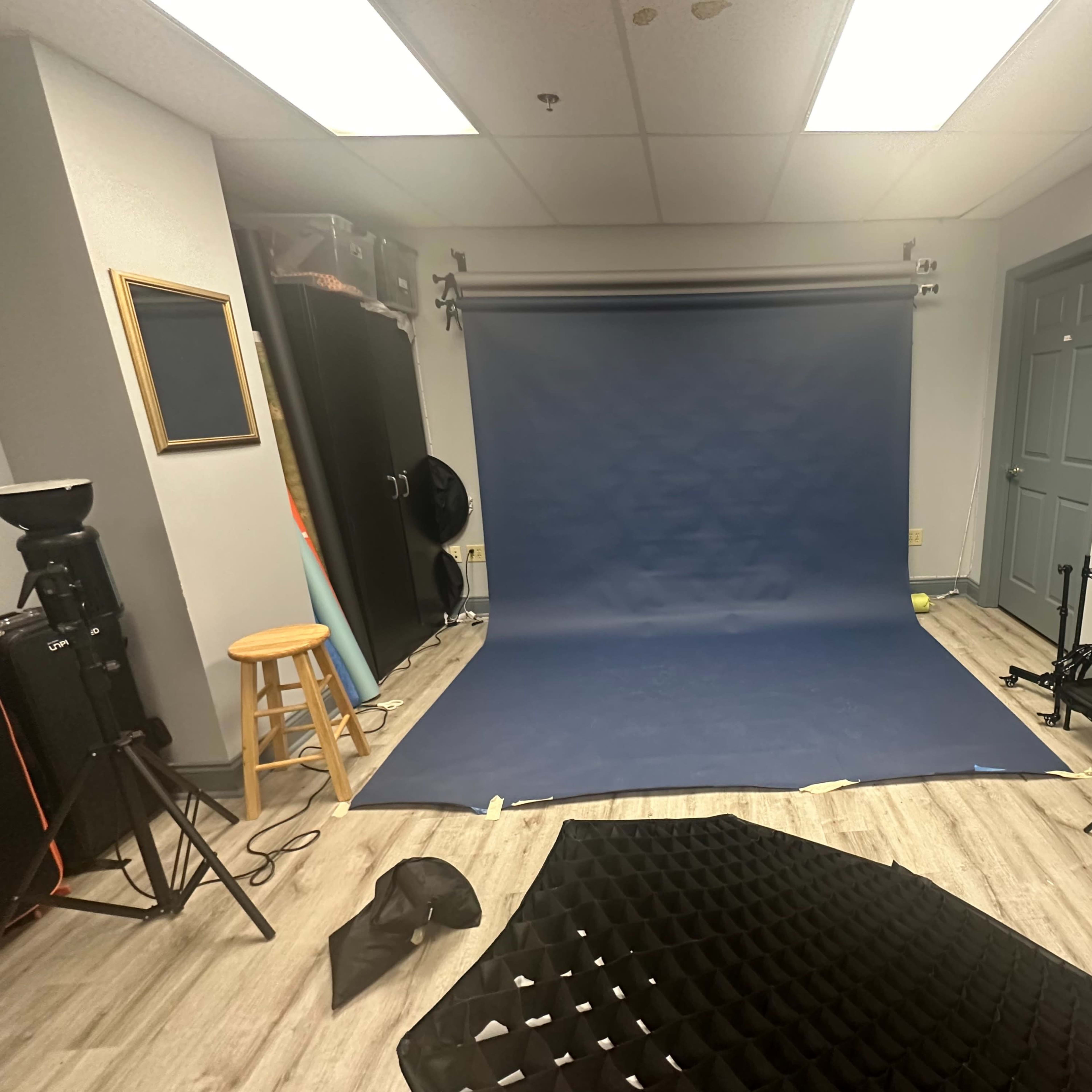 A photography studio with a blue backdrop, lighting equipment, and various props arranged on the floor.