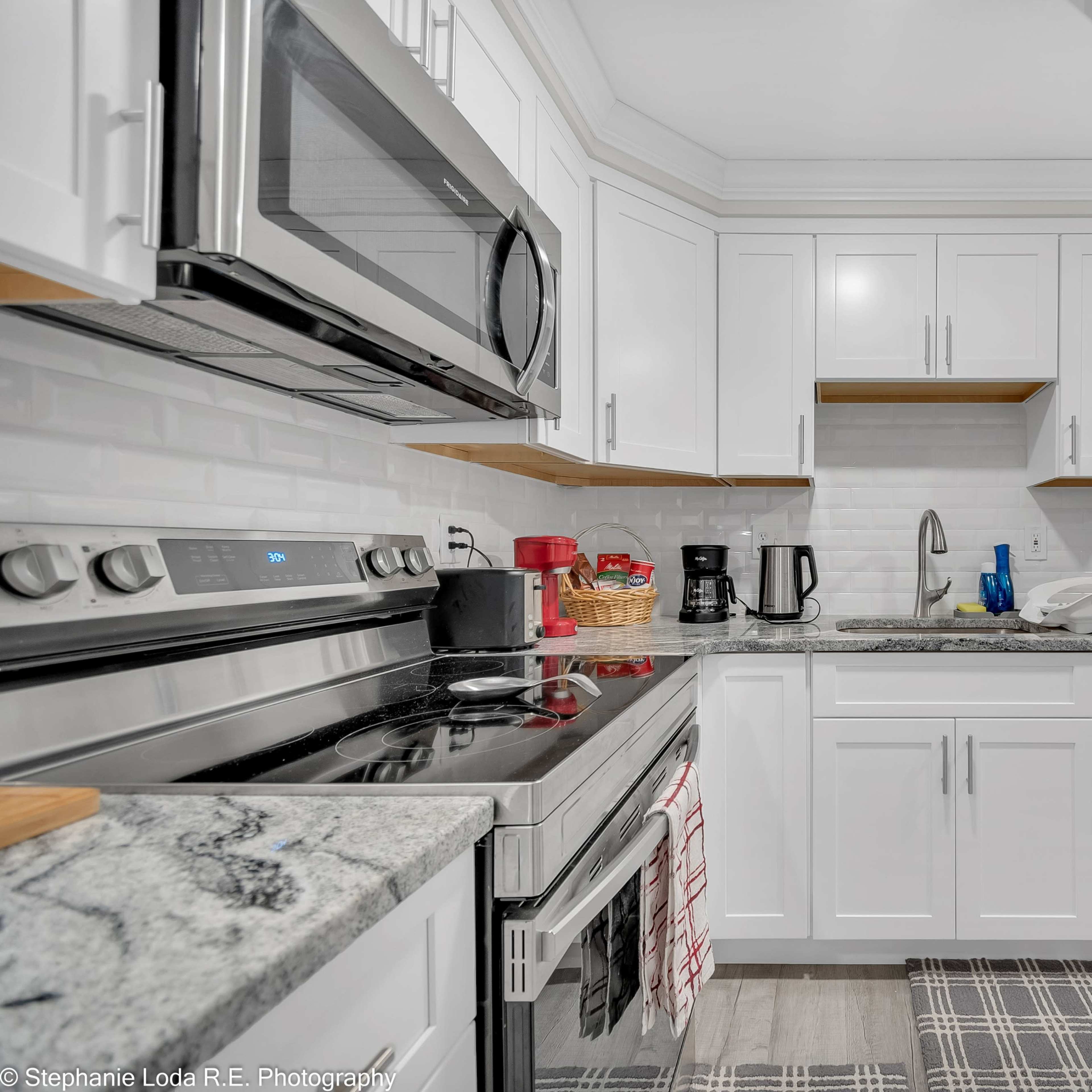 A modern kitchen with white cabinetry, stainless steel appliances, and a gray countertop.