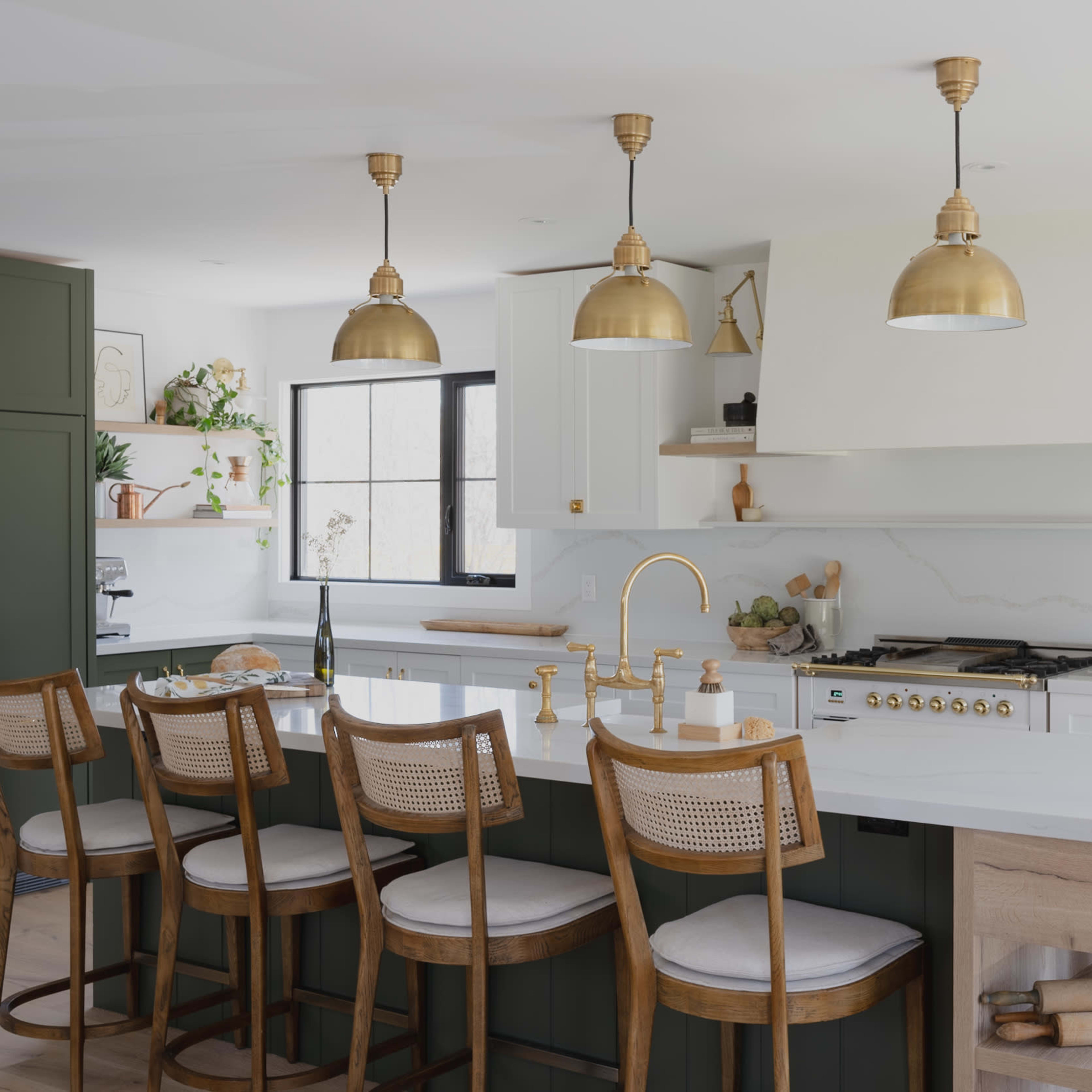 A modern kitchen features green and white cabinetry, gold pendant lighting, and a large island with wooden chairs.