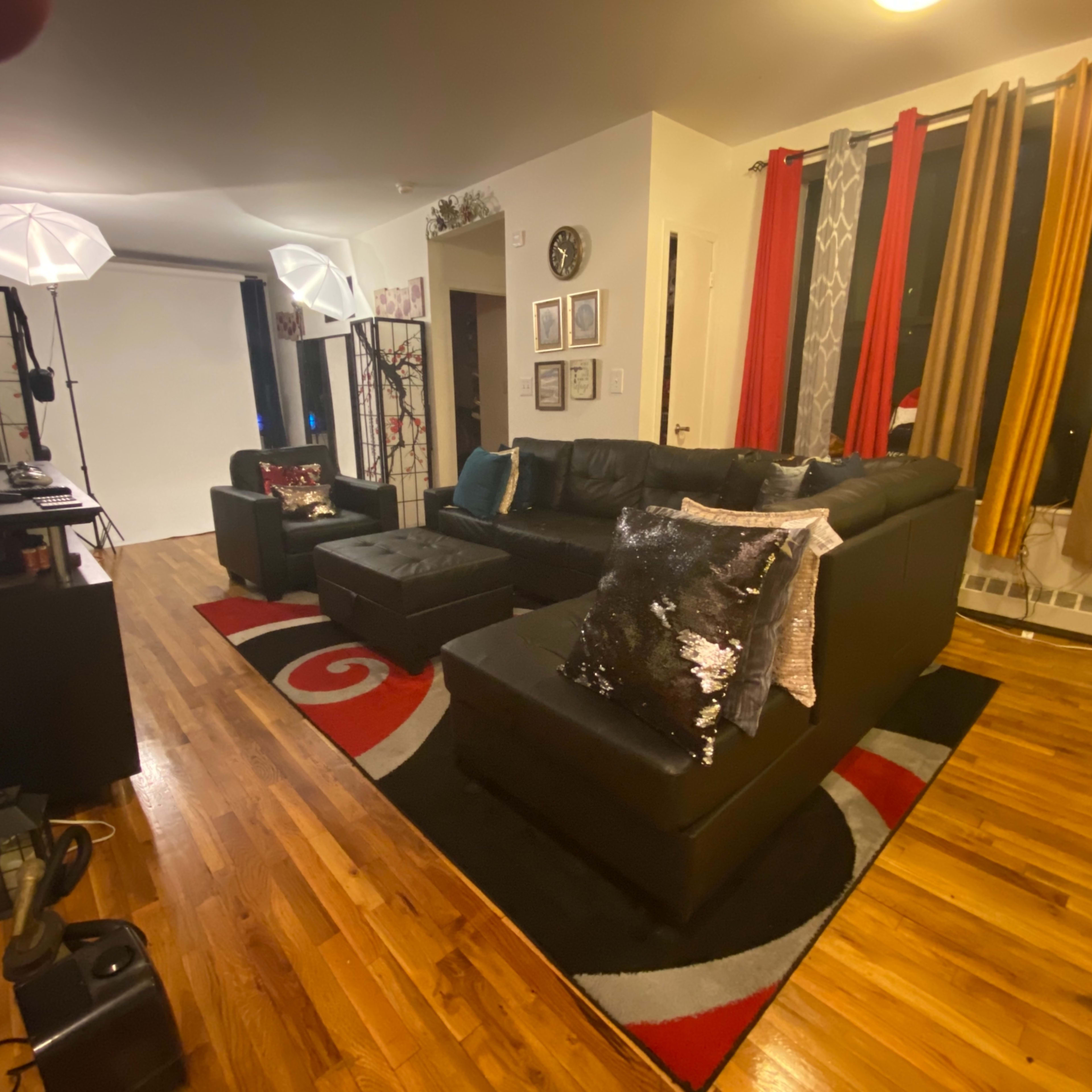 A living room with a black sectional sofa, colorful curtains, and a modern decorative rug on a wooden floor.