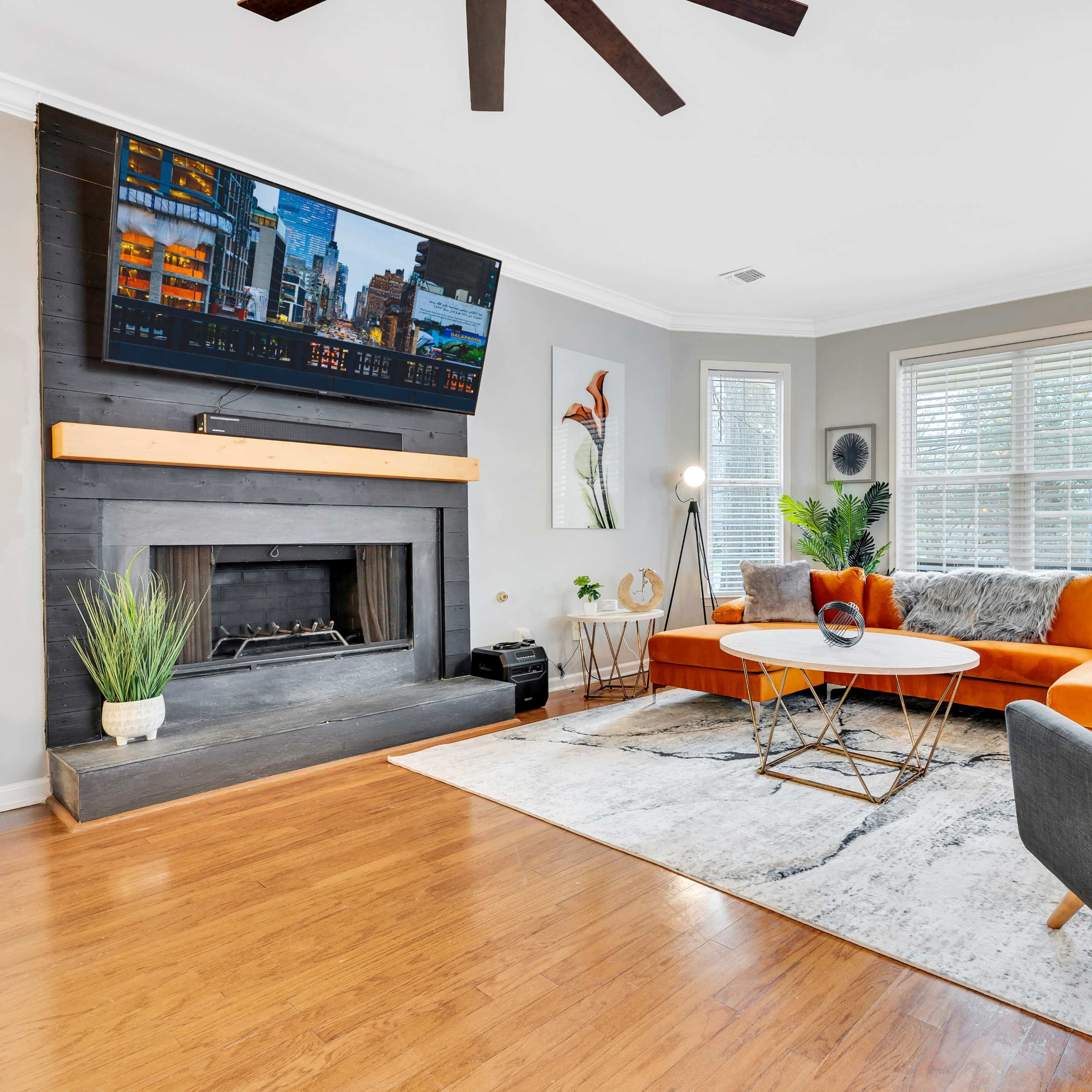 A living room with an orange sectional sofa, a round coffee table, a modern chair, and a flat-screen TV mounted above a fireplace.