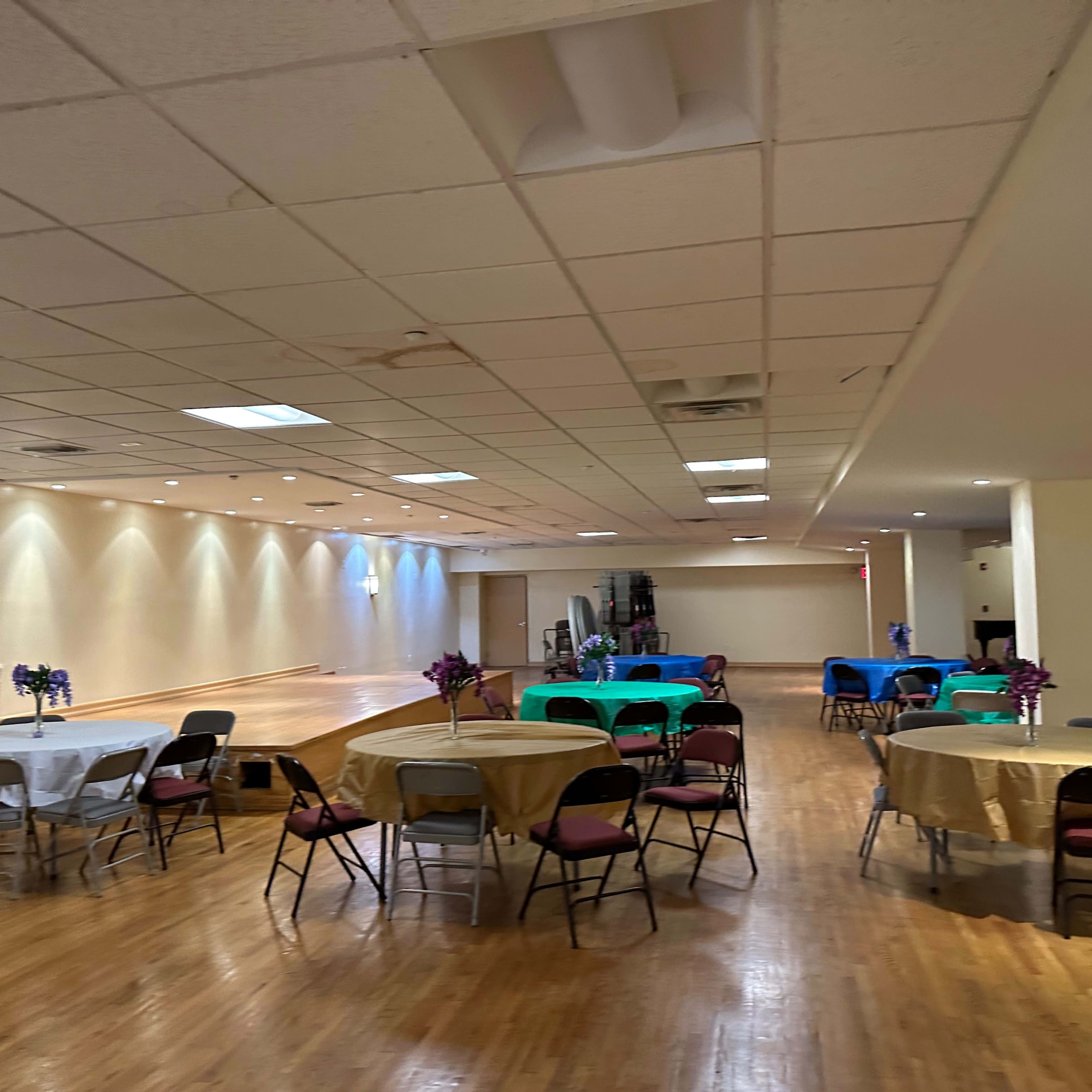 A spacious event hall with several tables covered in colorful linens arranged around a polished wooden floor.