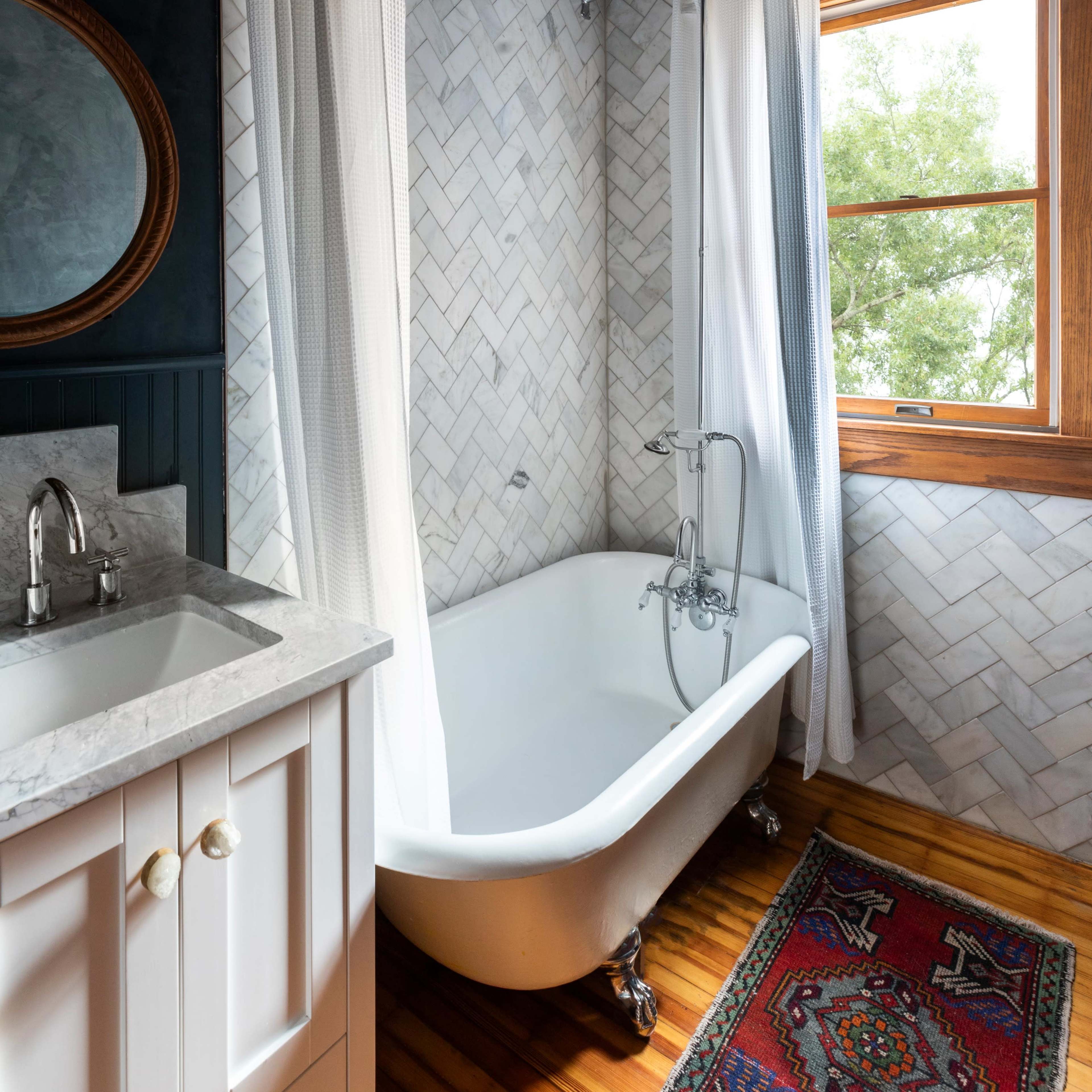 A bathroom with a clawfoot tub beneath a shower curtain, a marble sink, and a window that allows natural light to enter.