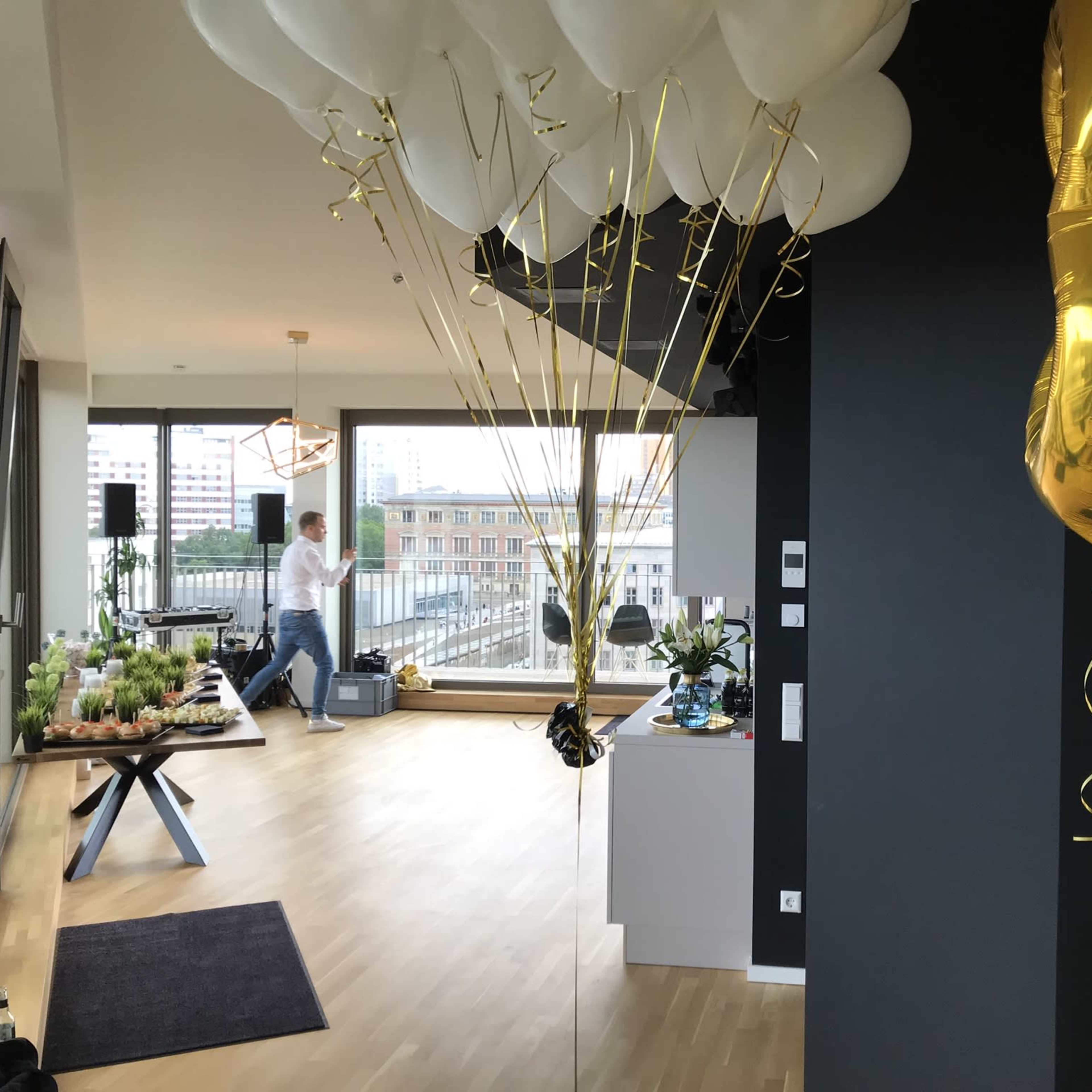 A modern event space with balloons tied to a table, a person in the background, and a view of a city through large windows.