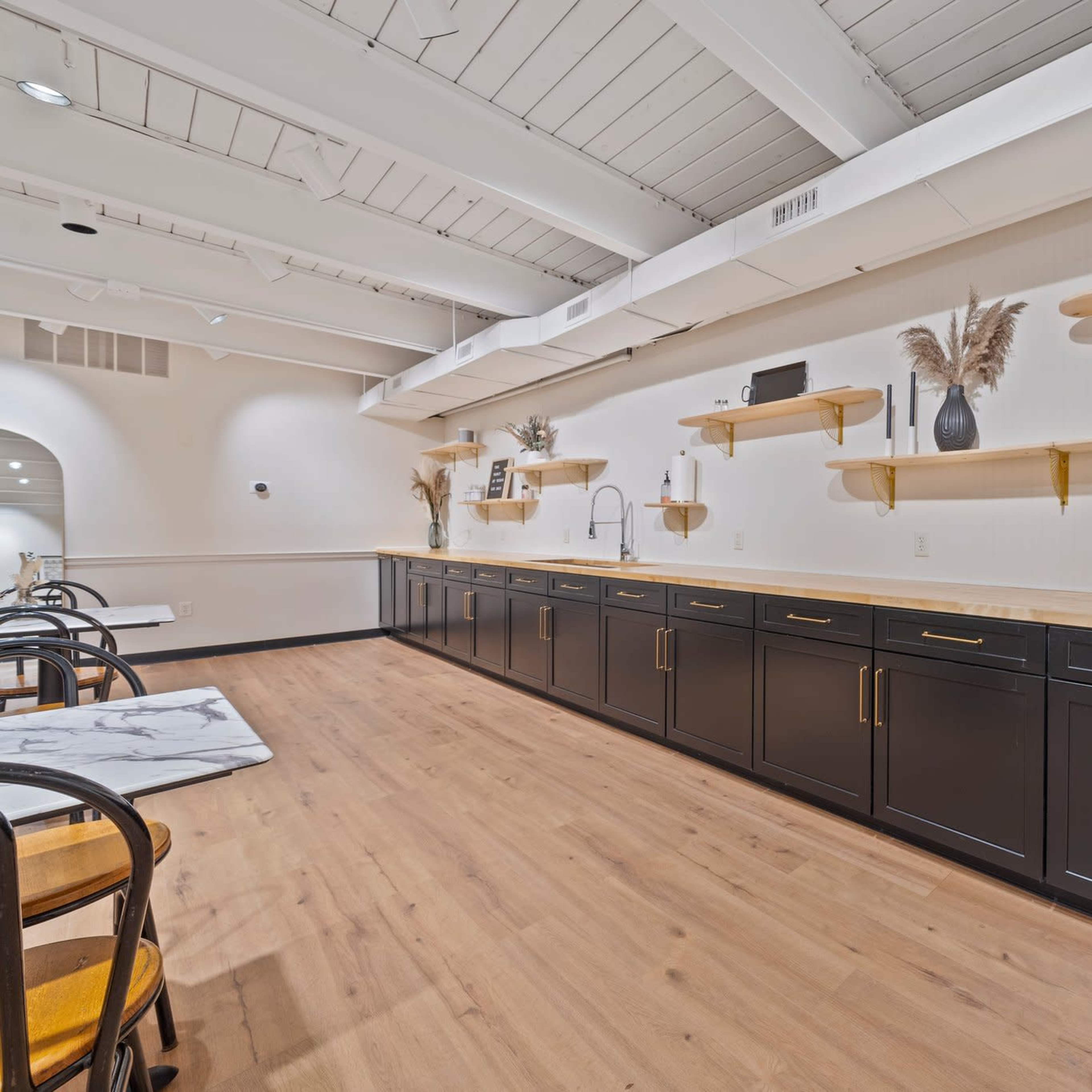 A modern kitchen with a long countertop, dark cabinets, and wooden shelves mounted on a light wall.