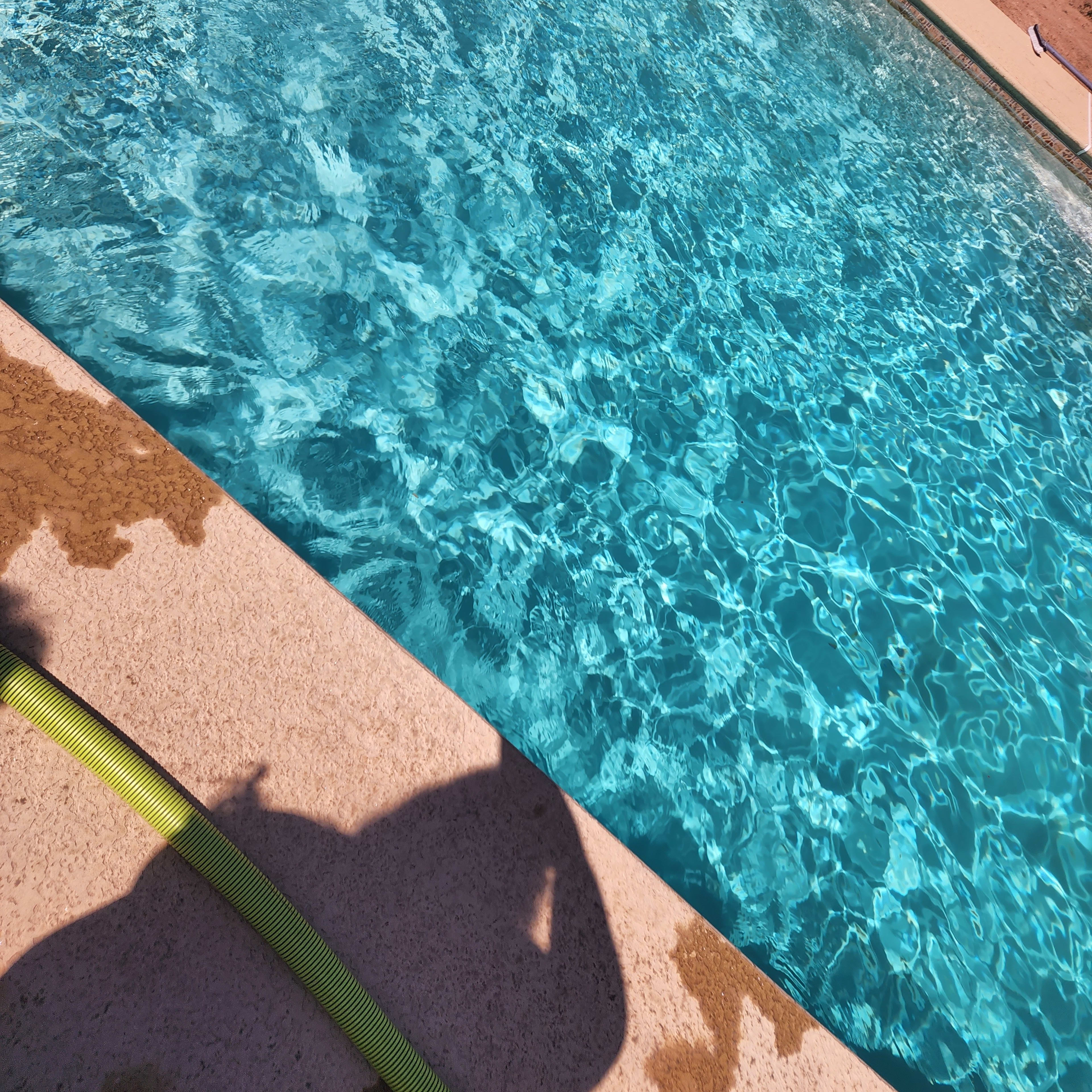 A clear swimming pool with sunlight reflecting off the water's surface and a shadow of a person beside it.