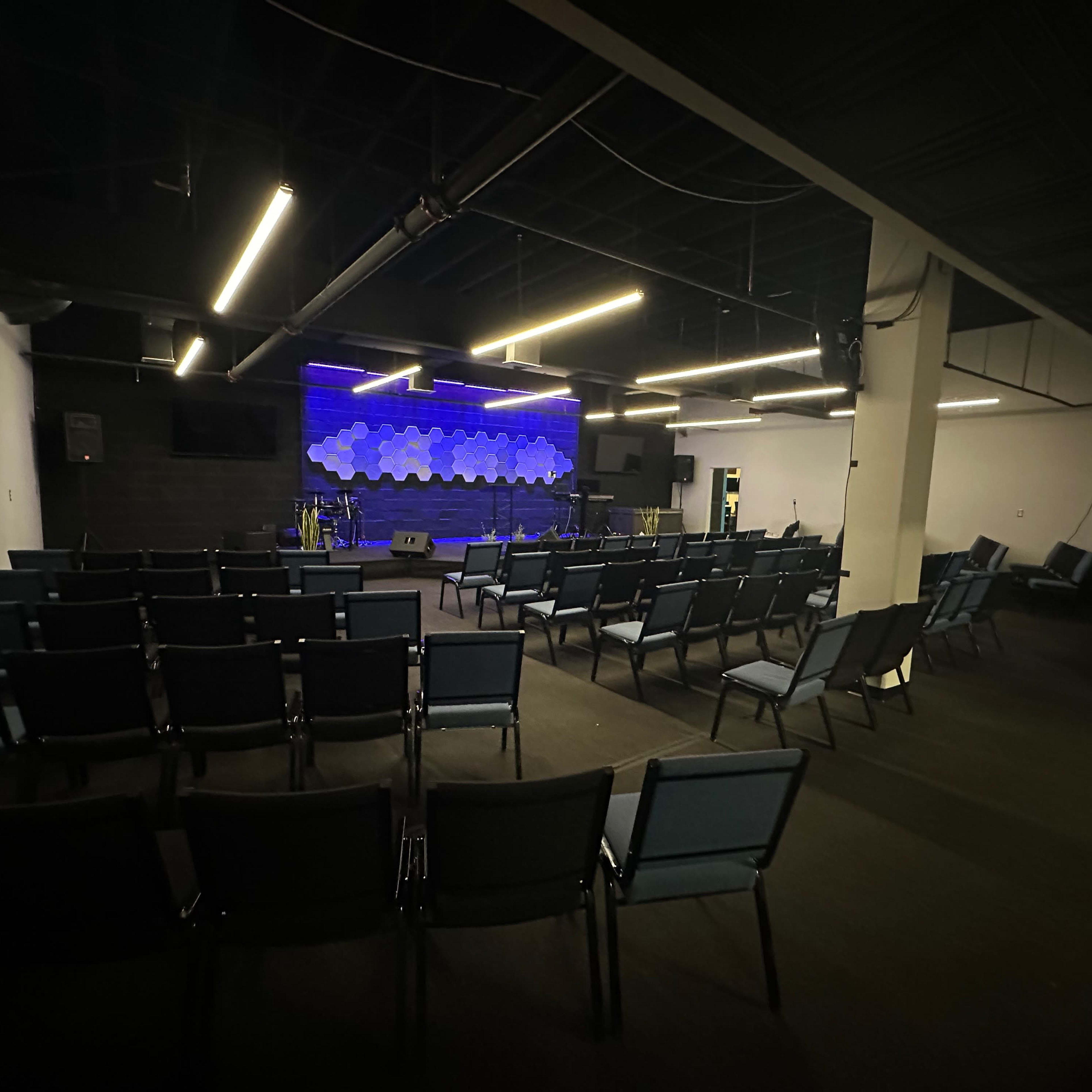 A spacious auditorium with rows of chairs facing a lit stage that features a decorative backdrop.