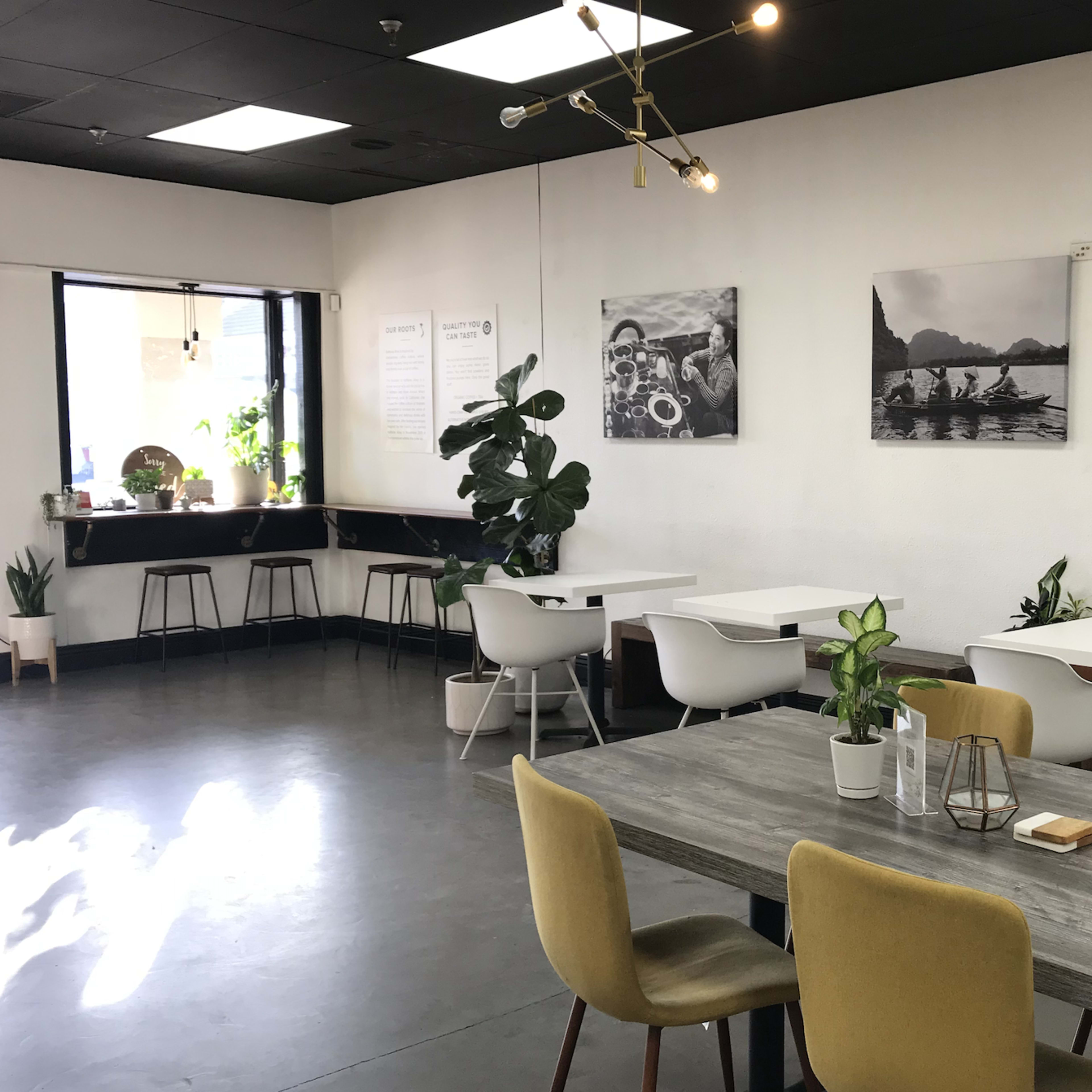 A modern café interior with several tables, plants, and framed photographs on the walls.