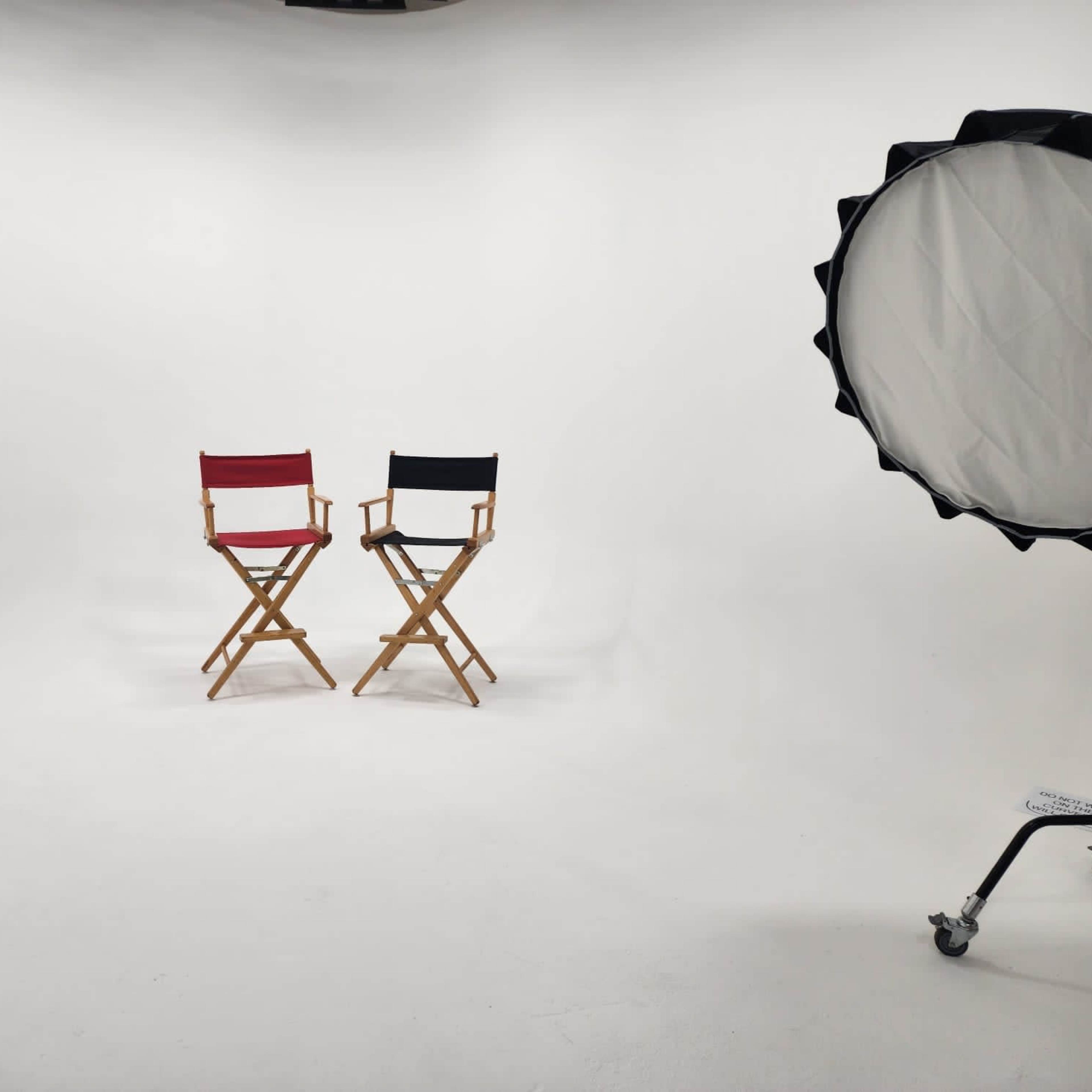Two wooden director's chairs, one red and one black, positioned in a well-lit studio with a plain white background.