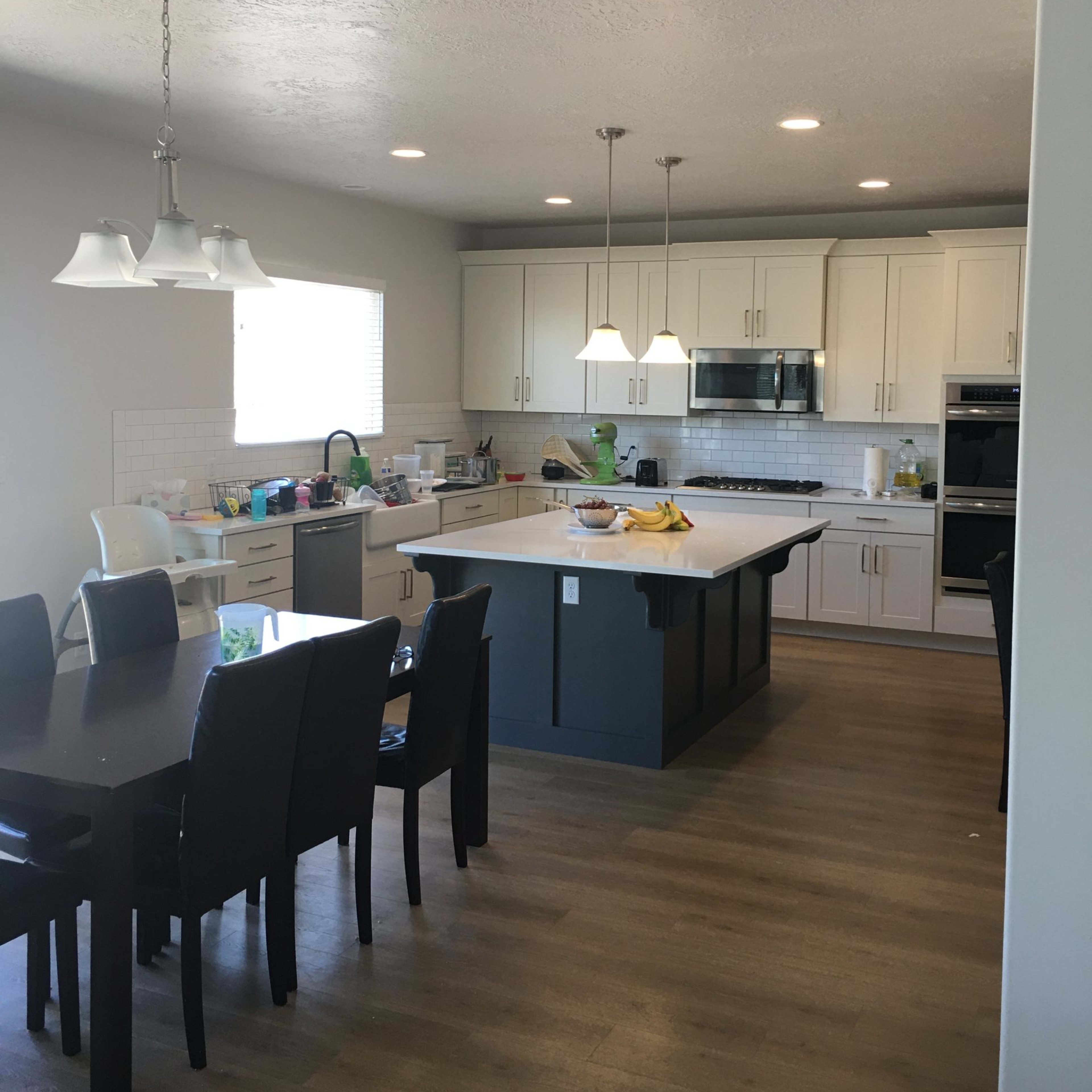 A modern kitchen features white cabinets, a central island, and a dining area with a dark wooden table and chairs.