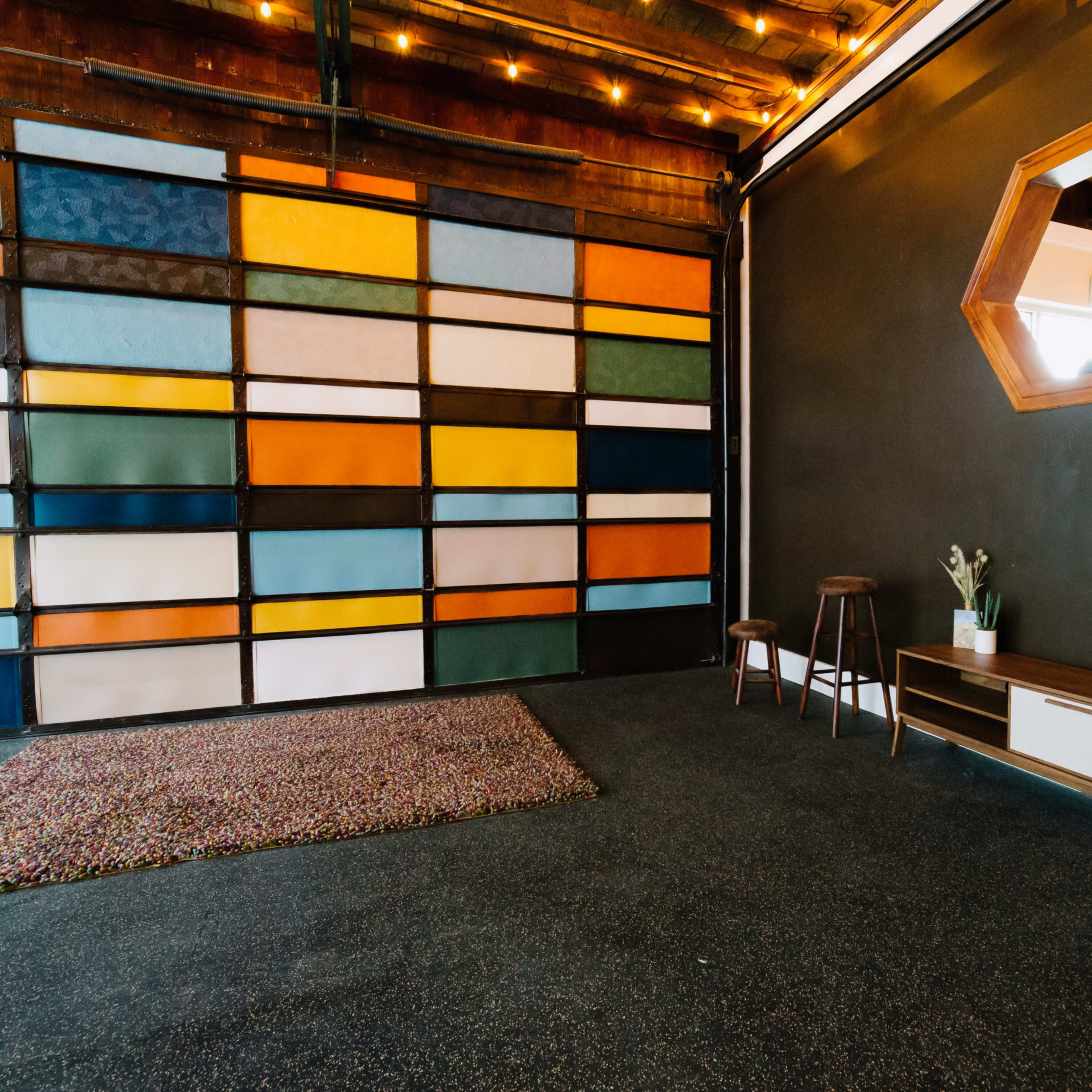 An interior space featuring a colorfully patterned wall, a dark floor, a mirror, a small wooden table, a plant, and a rug.