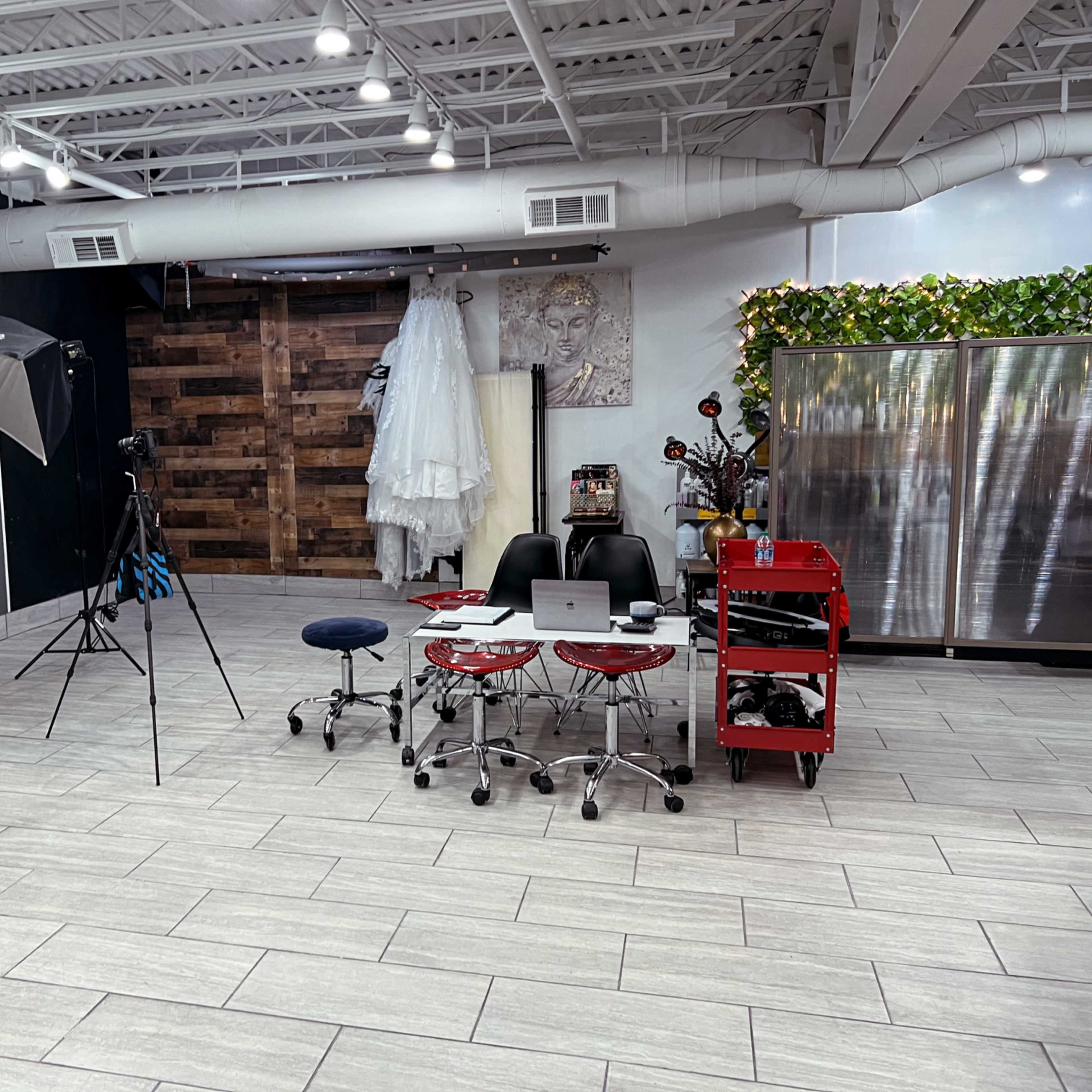A spacious studio setup featuring photography equipment, a laptop on a table, two red chairs, and a backdrop with a decorative wooden wall.