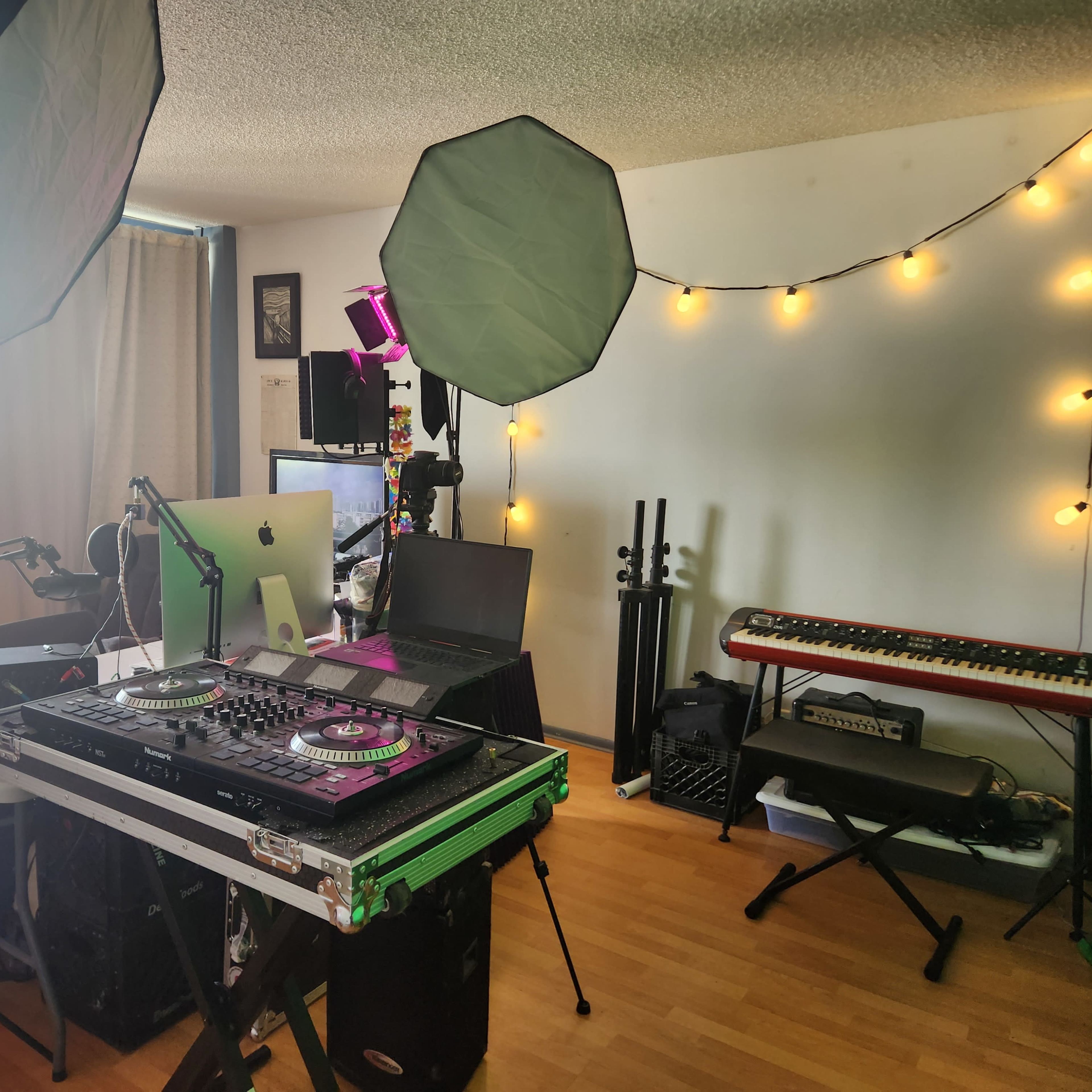 A home recording studio with a DJ setup, computer, lighting equipment, and musical instruments arranged in a well-lit room.