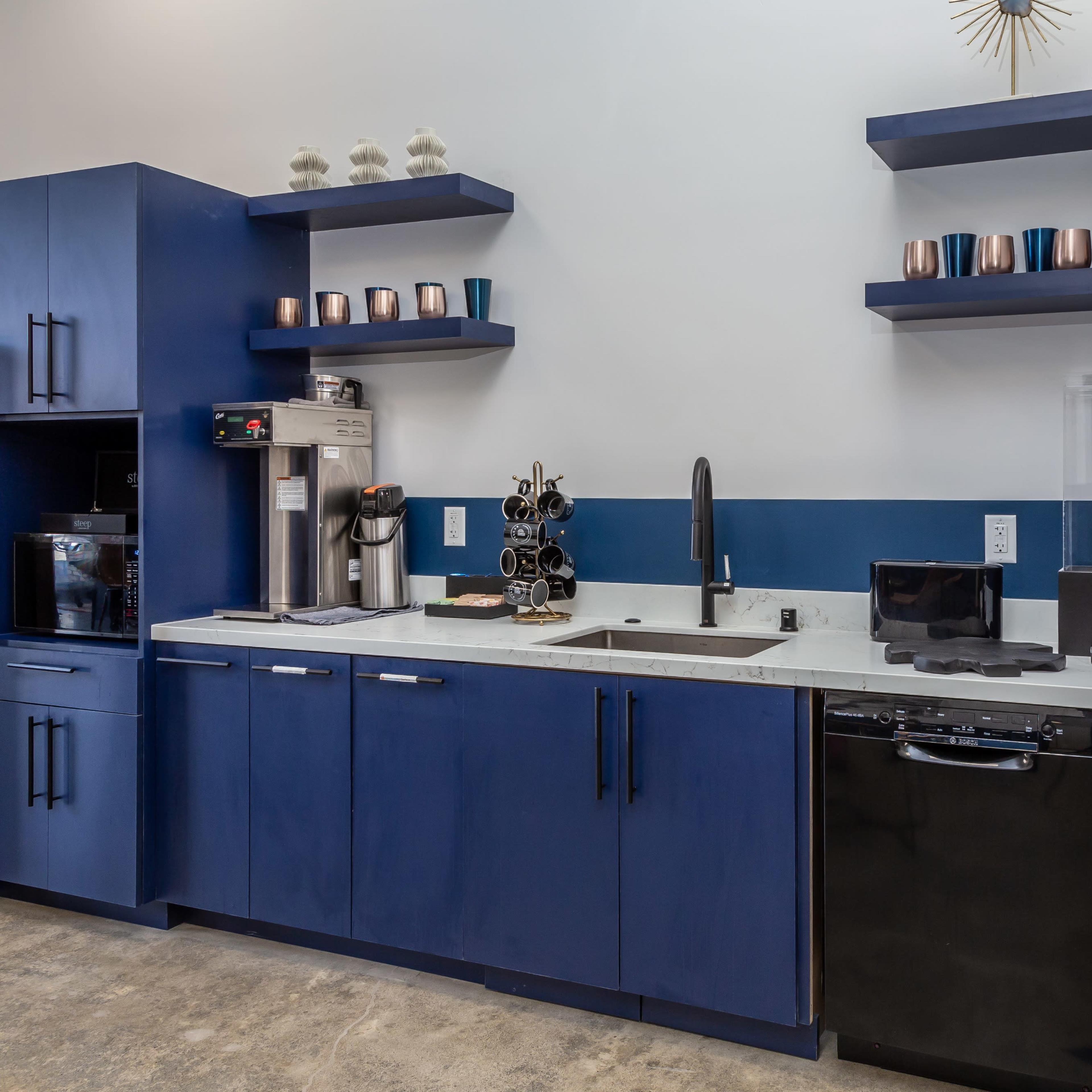 A modern kitchen area featuring blue cabinetry, a stainless steel sink, a coffee machine, and a microwave on the counter.