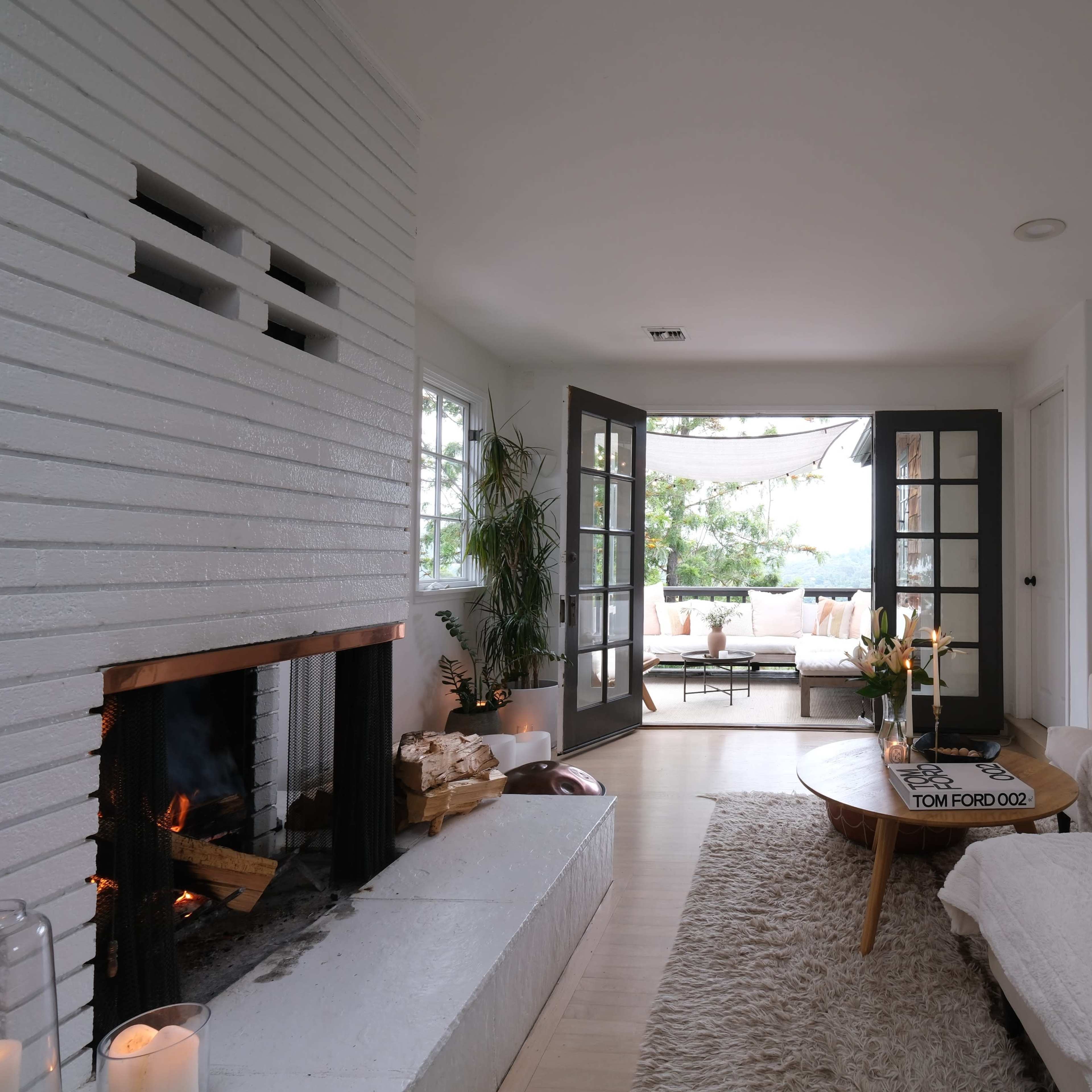 A modern living room with a white brick fireplace, a large sectional sofa, and a set of double doors leading to a patio area.