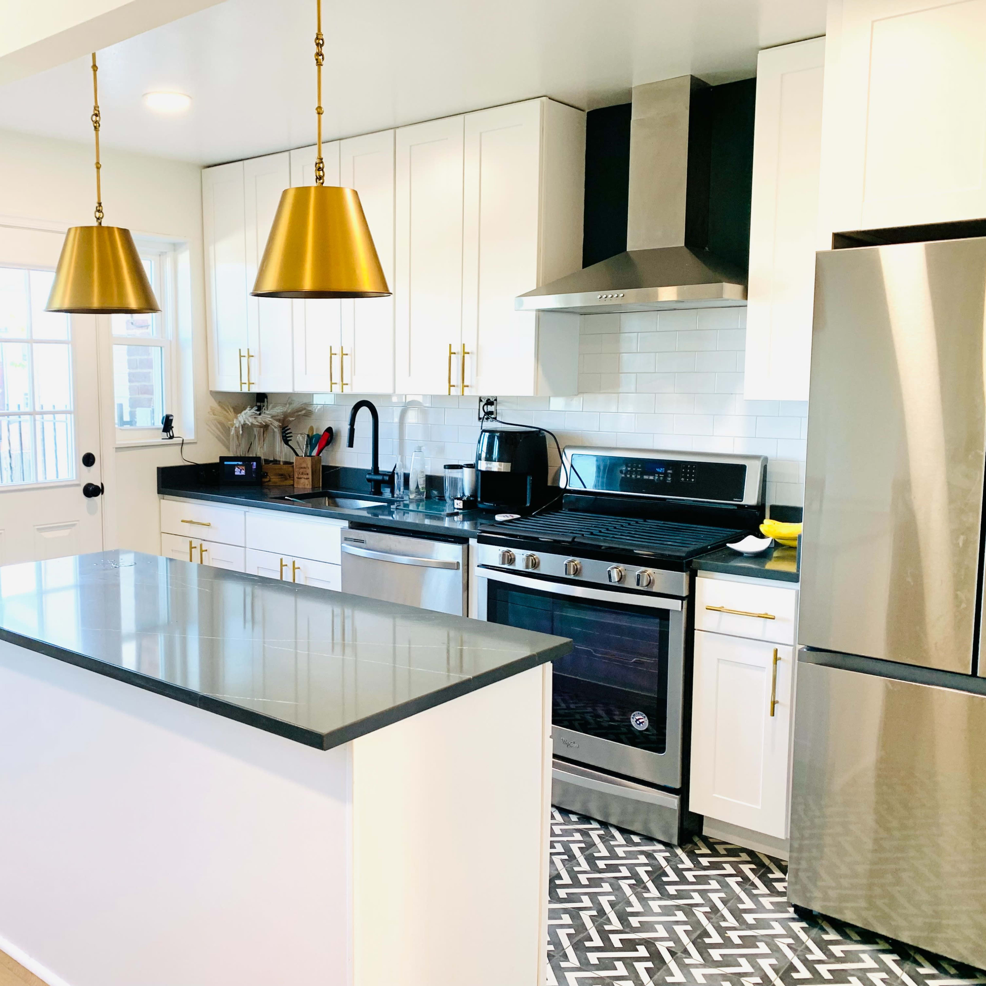 A modern kitchen with white cabinetry, a stainless steel stove, and a center island featuring gray countertops and two gold pendant lights above.