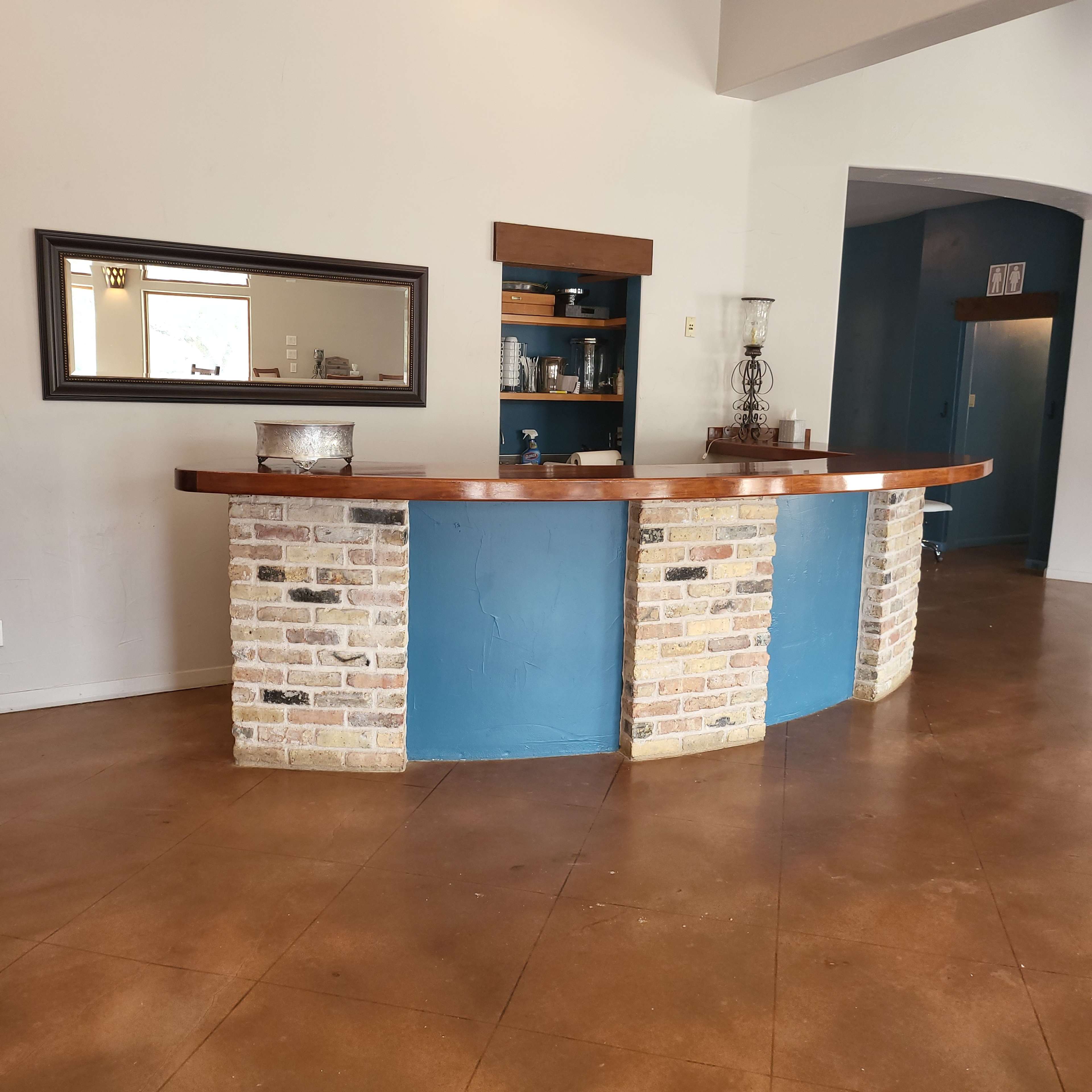 A reception desk with a curved design, featuring a brick base and a blue painted front, set in a spacious interior with polished concrete flooring.