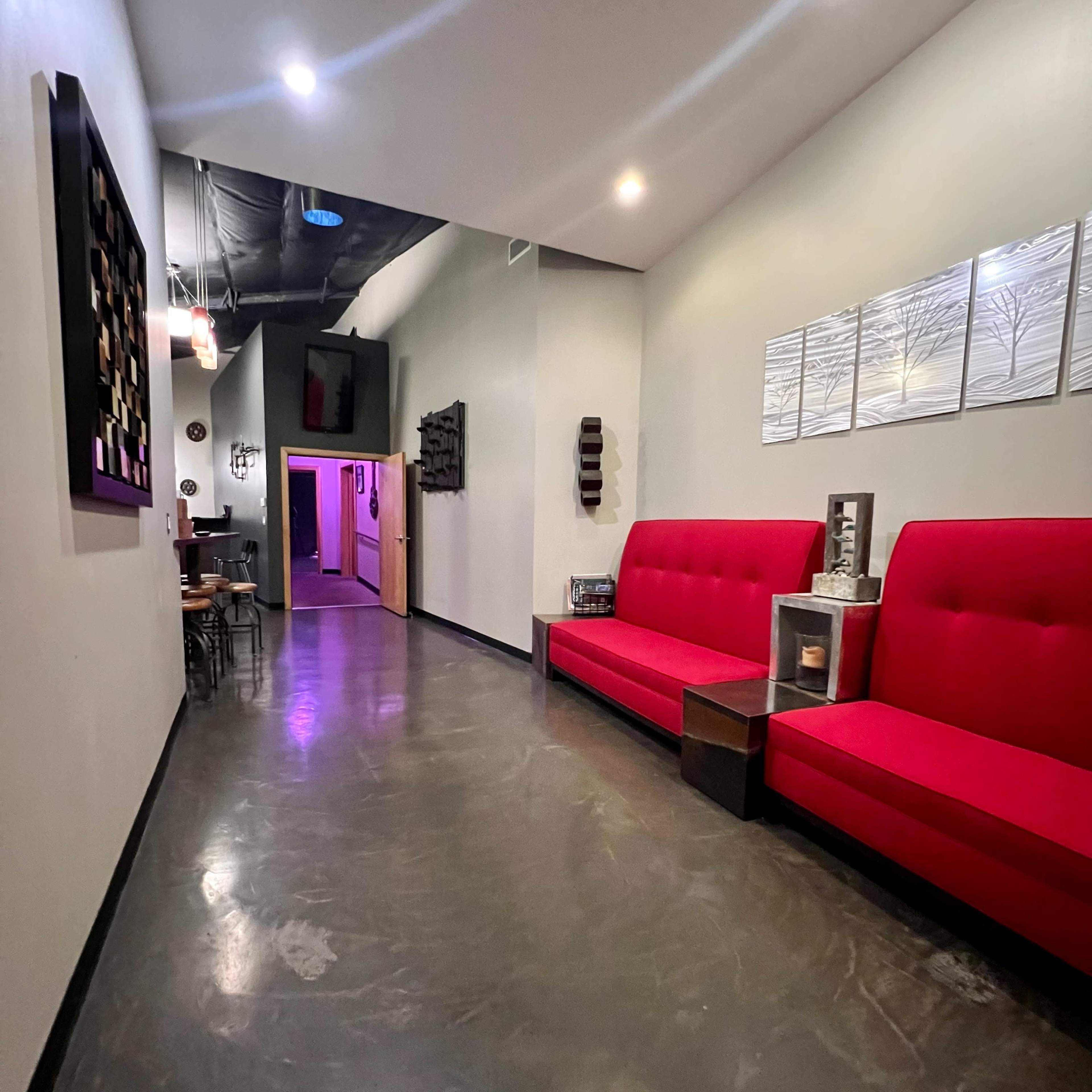 A hallway with red seating on either side, leading to a doorway illuminated by purple light at the far end.