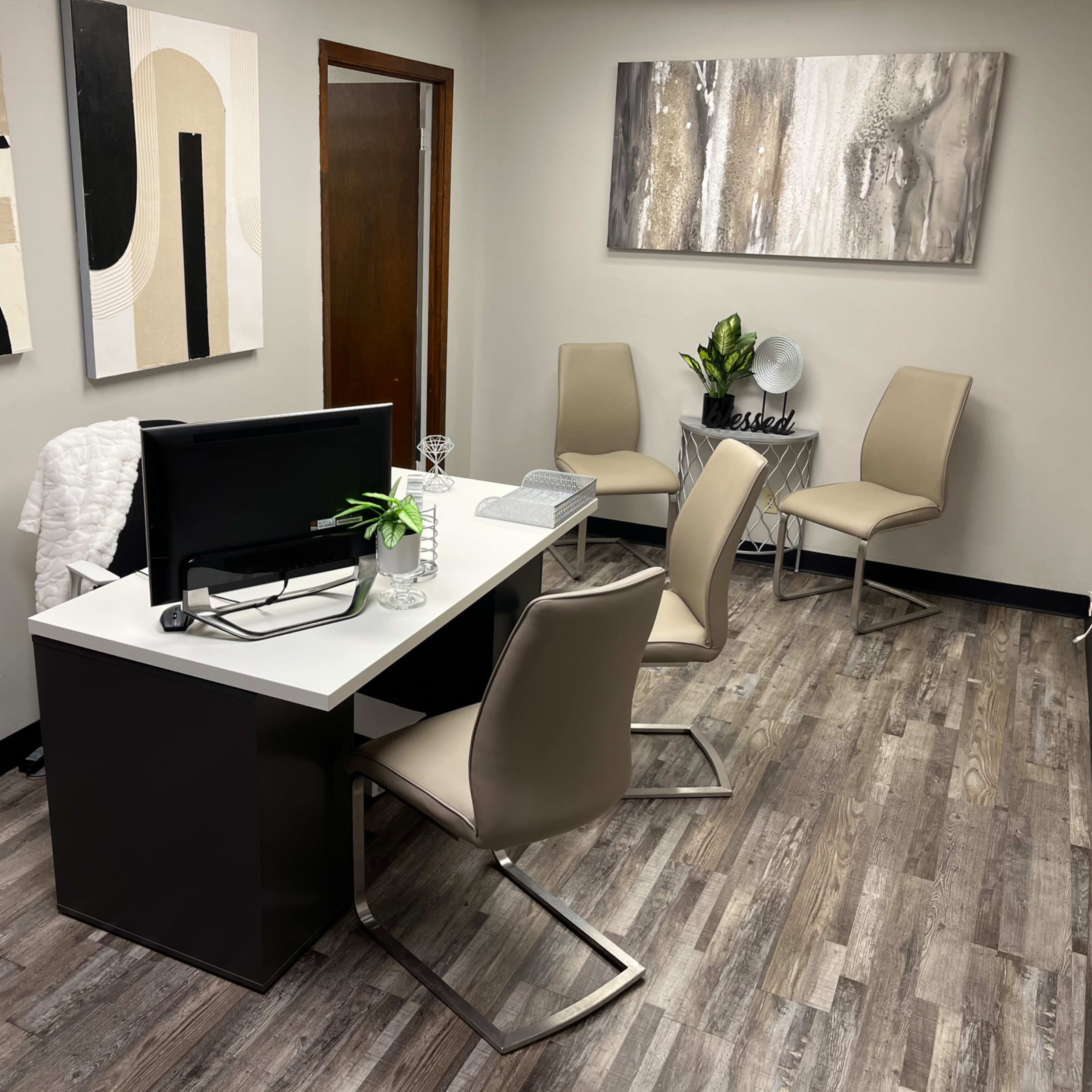 A modern office with a white desk, a computer, four chairs, and abstract wall art.