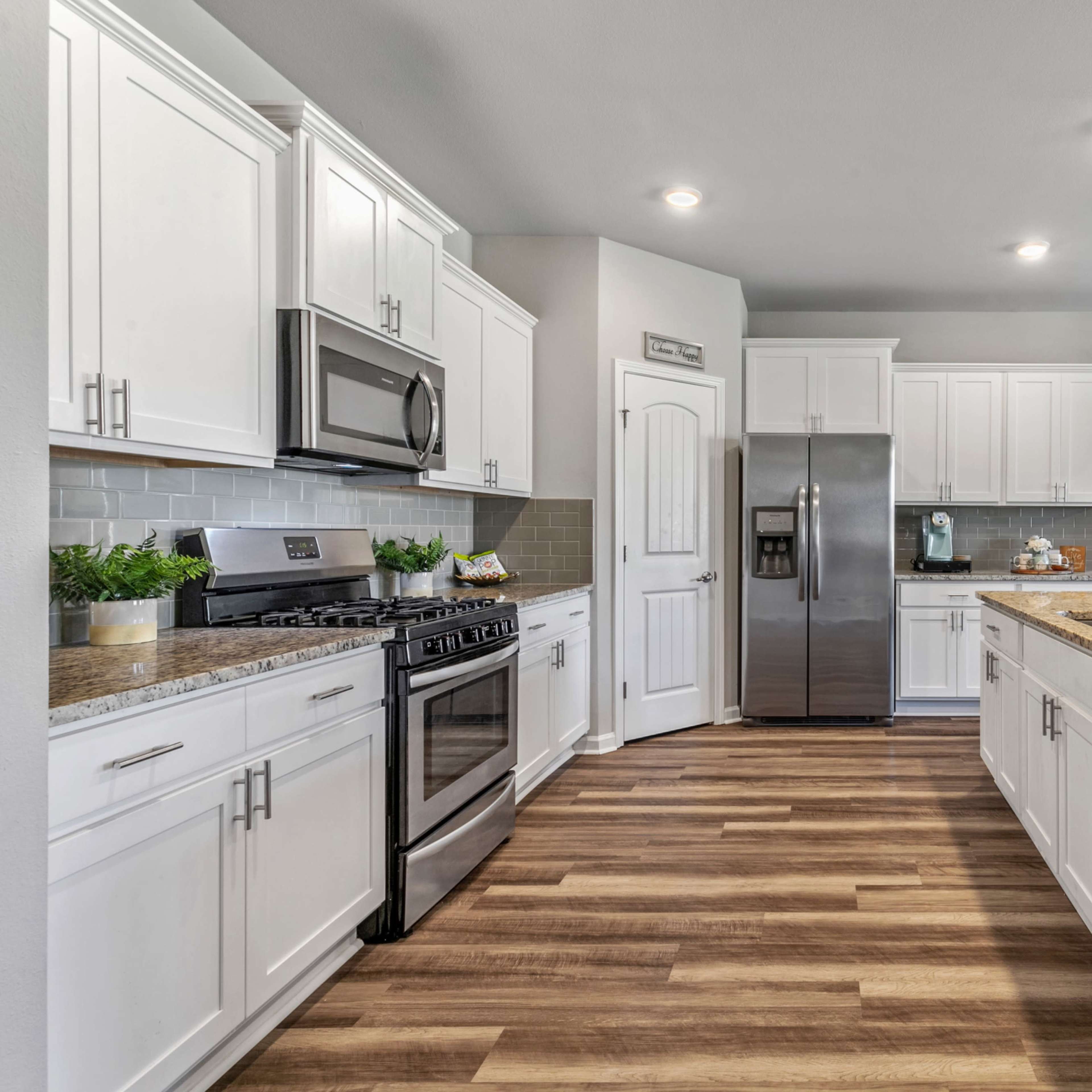 A modern kitchen with white cabinets, stainless steel appliances, and a granite countertop, featuring a central island and hardwood flooring.