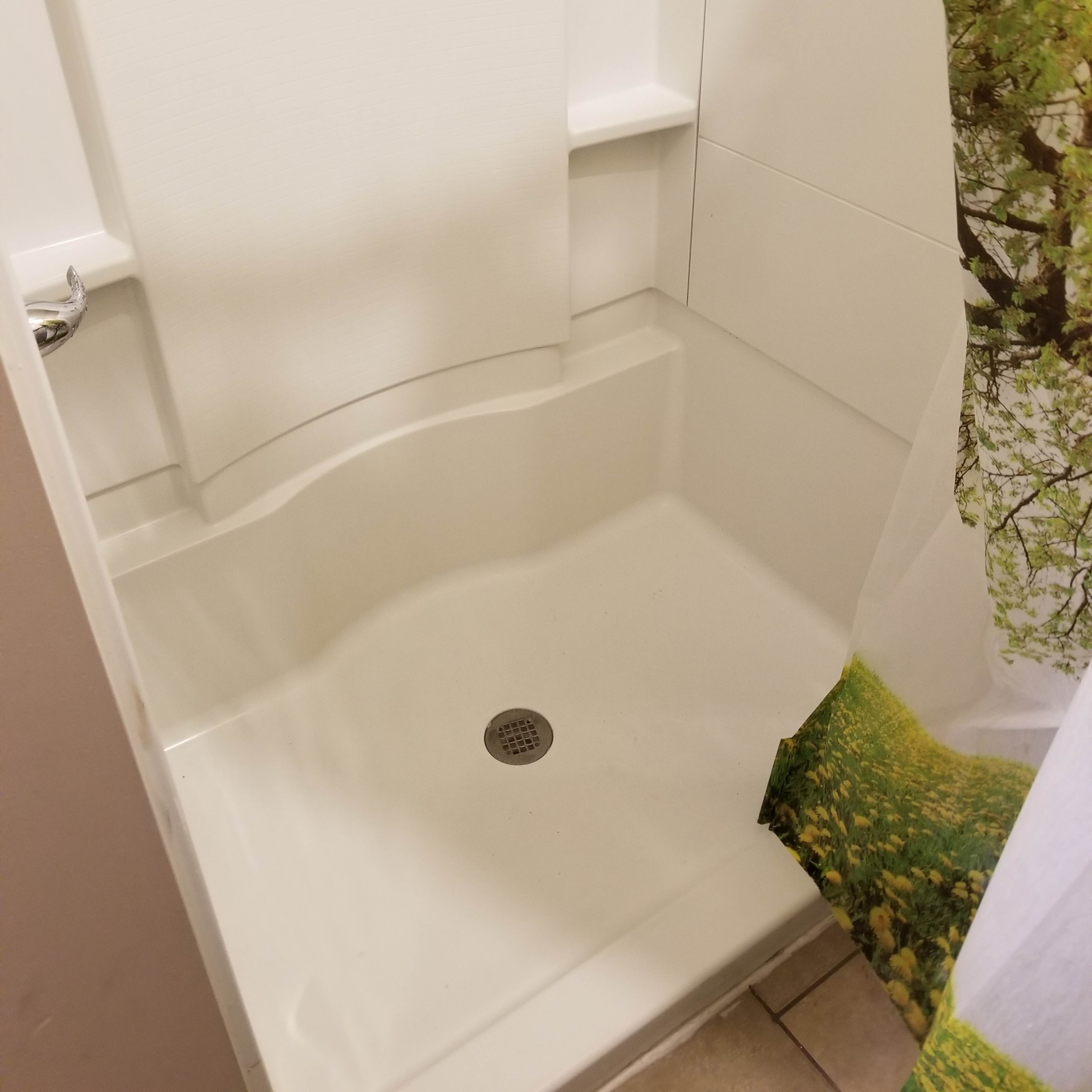 A corner shower stall with a white interior and a floral shower curtain partially covering the entrance.