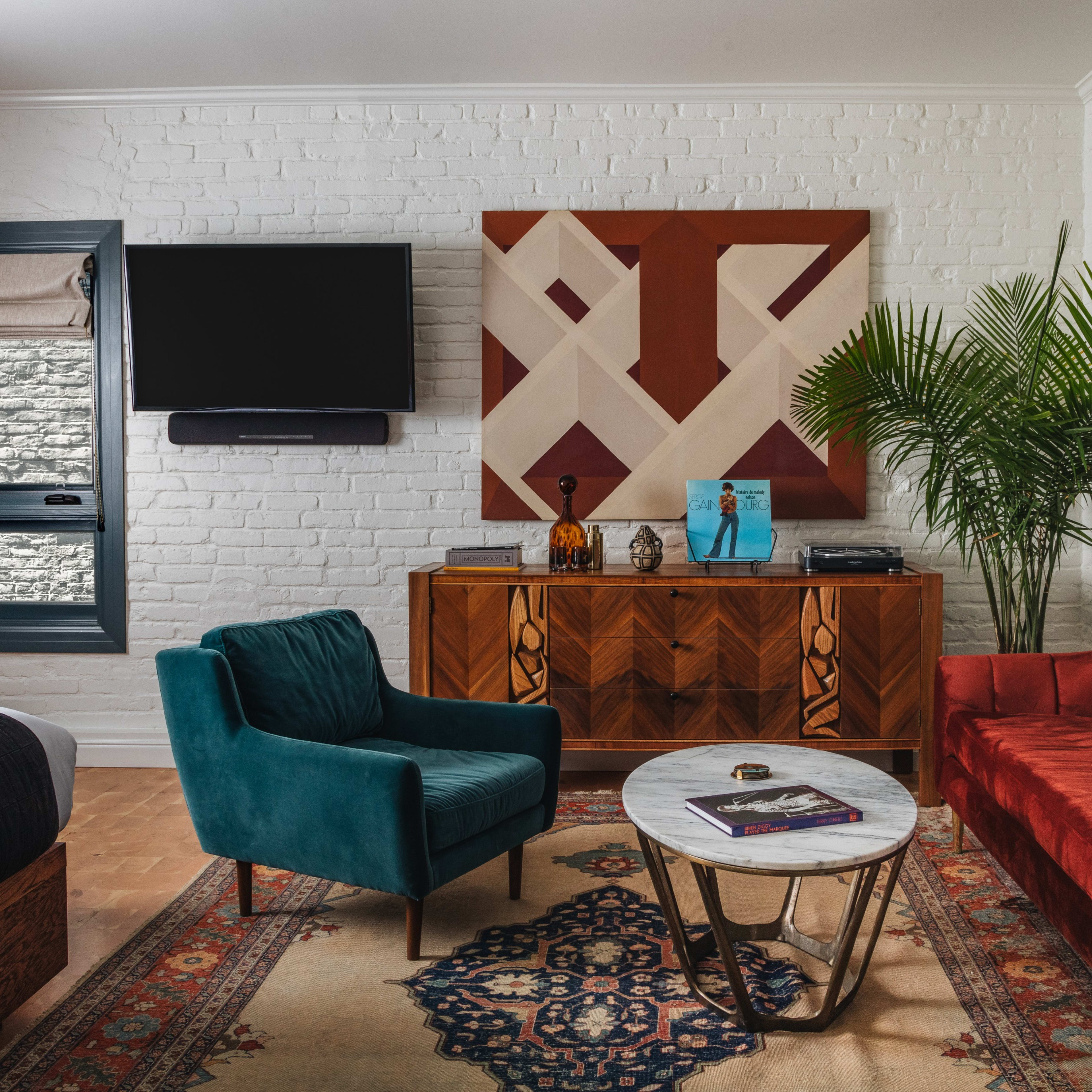 The room features a red sofa and a teal chair around a circular coffee table, with a large abstract artwork and a television mounted on the wall.