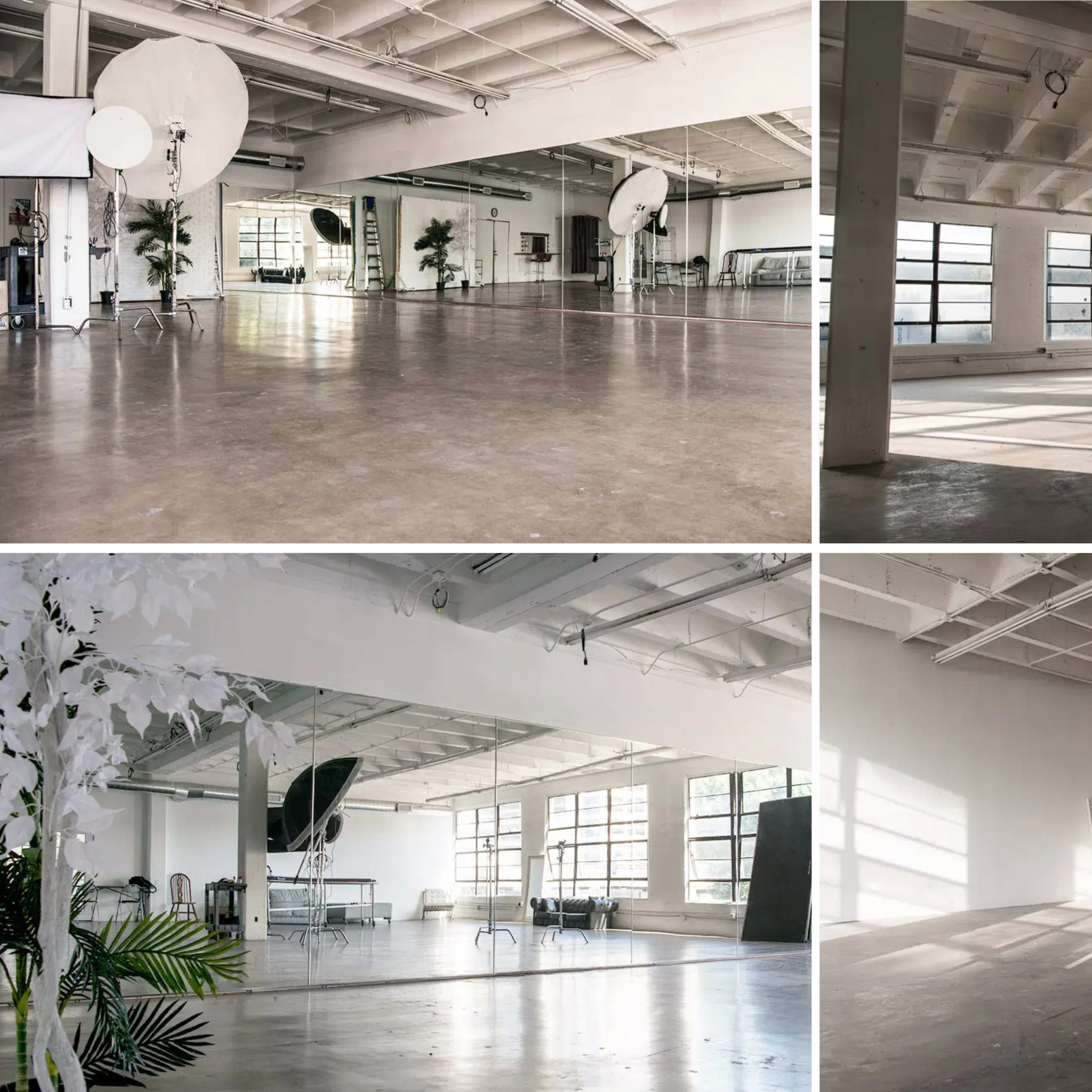 A spacious, well-lit studio with large windows, neutral-colored walls, and minimal furnishings in different sections.