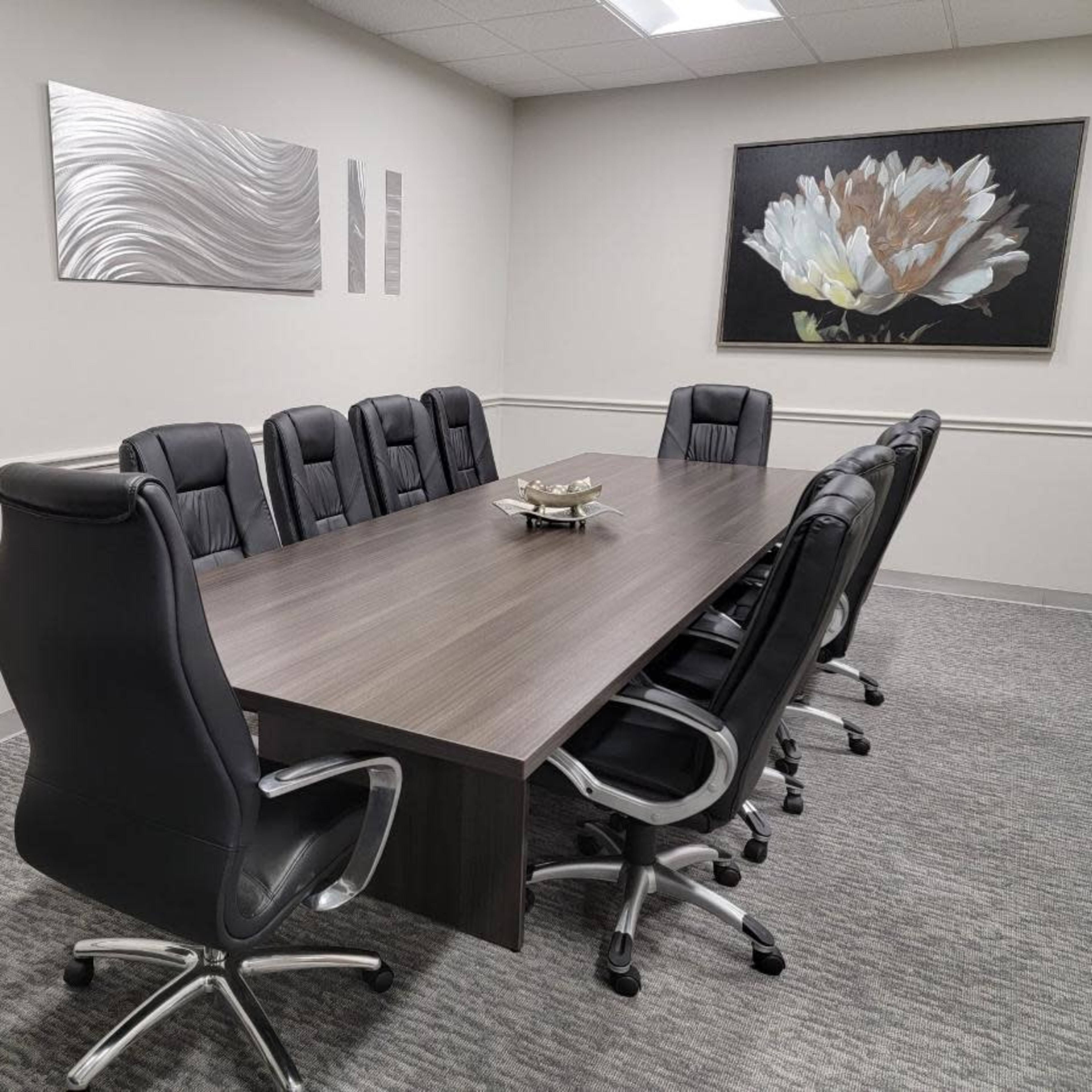 A conference room with a long rectangular table surrounded by black leather chairs and wall art featuring a flower.