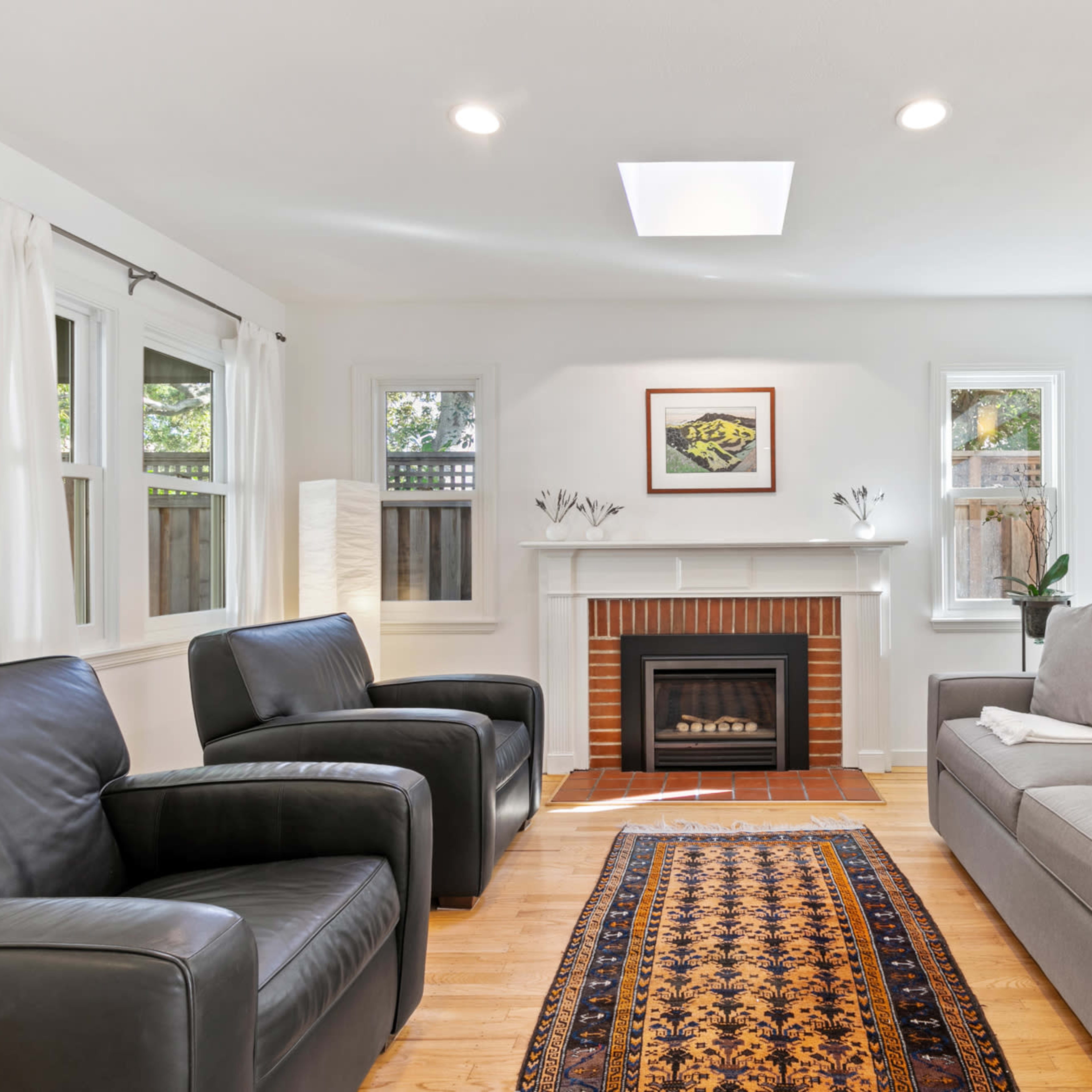A modern living room featuring a fireplace, two armchairs, a gray sofa, hardwood floors, and a decorative area rug.