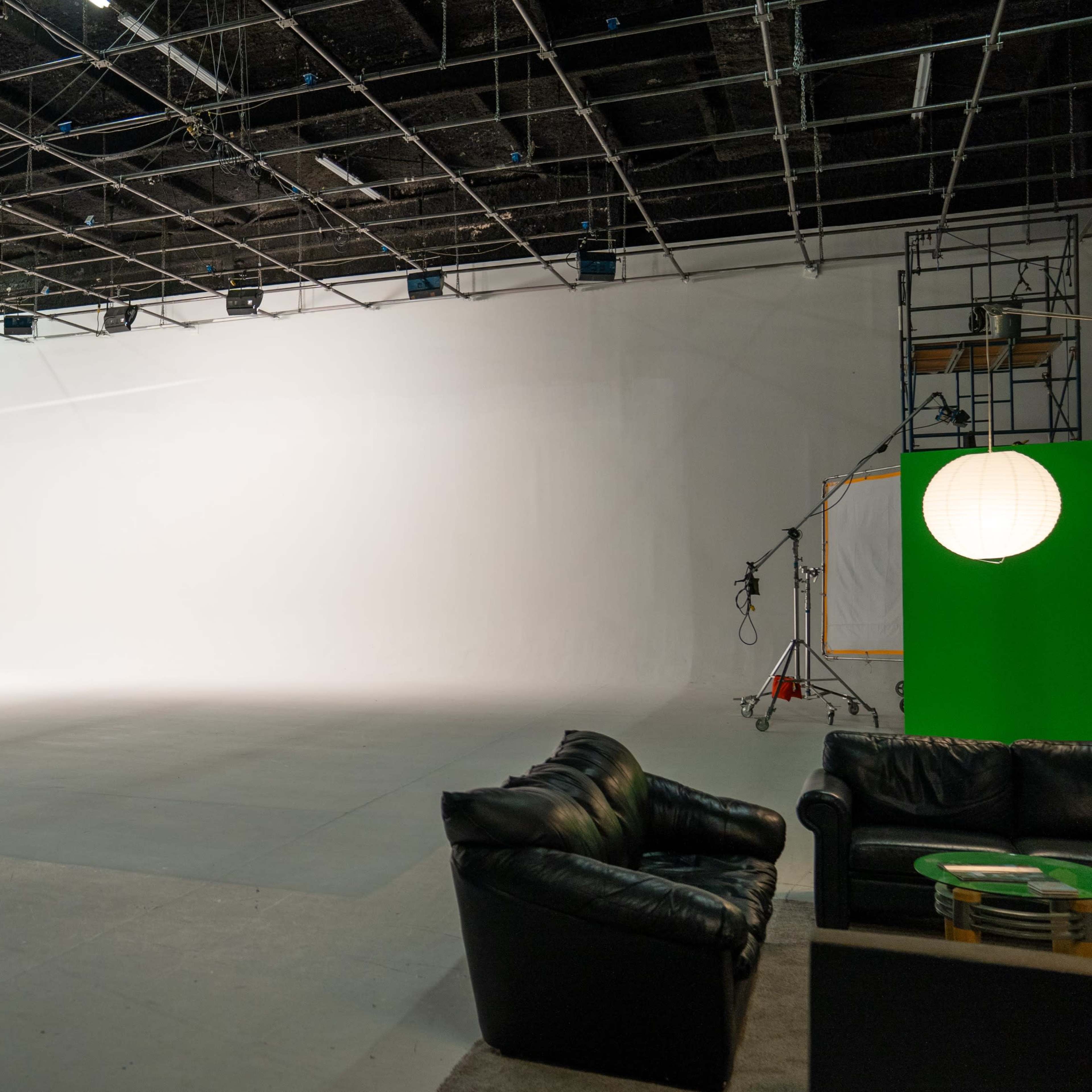 An empty studio space with a white backdrop and minimal furniture in the foreground.