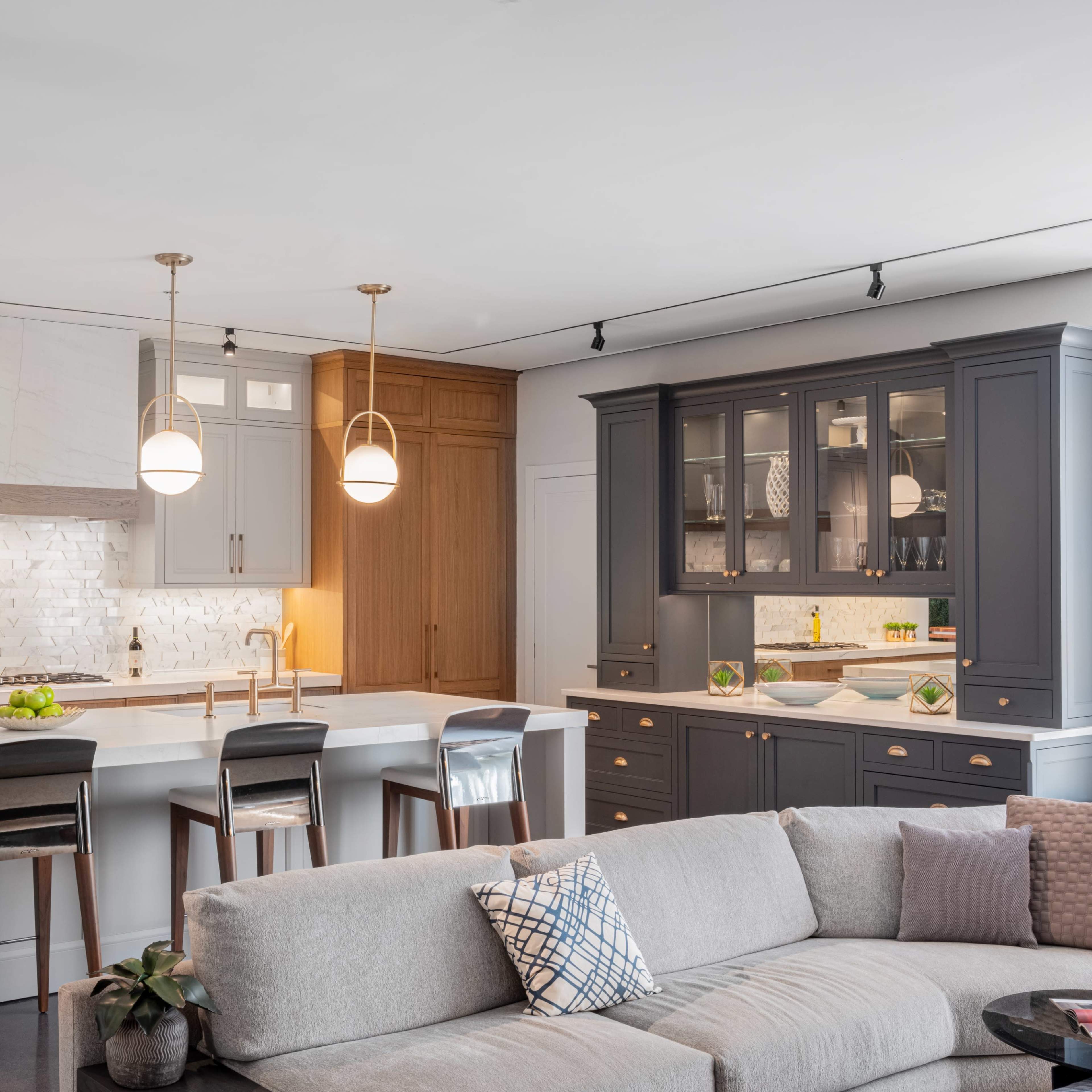 A modern kitchen features a large island with seating, wooden and gray cabinetry, pendant lighting, and a stylish backsplash.