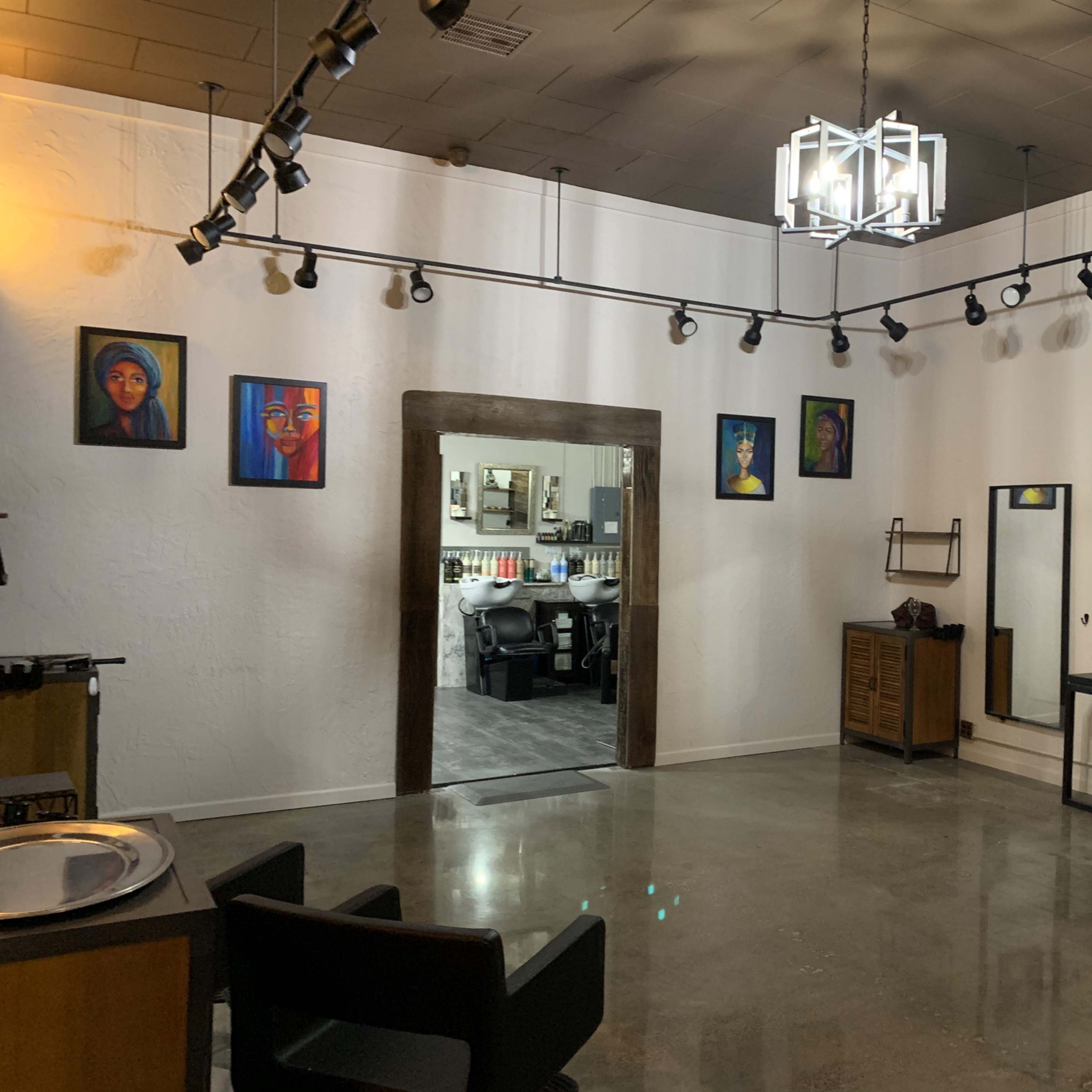 A modern hair salon with black chairs, a mirrored area, and artwork on the walls.