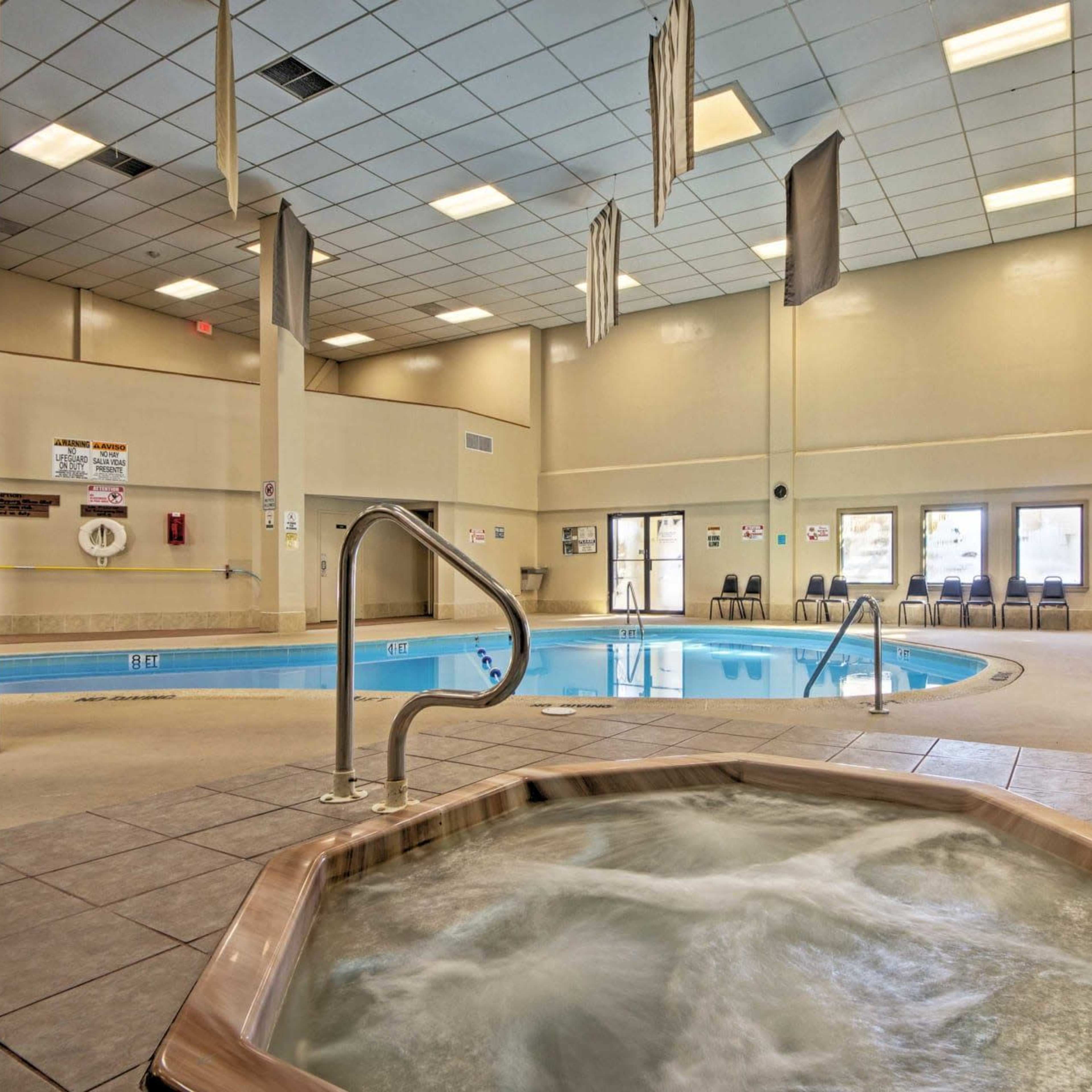 An indoor pool area with a hot tub in the foreground and seating along the walls.