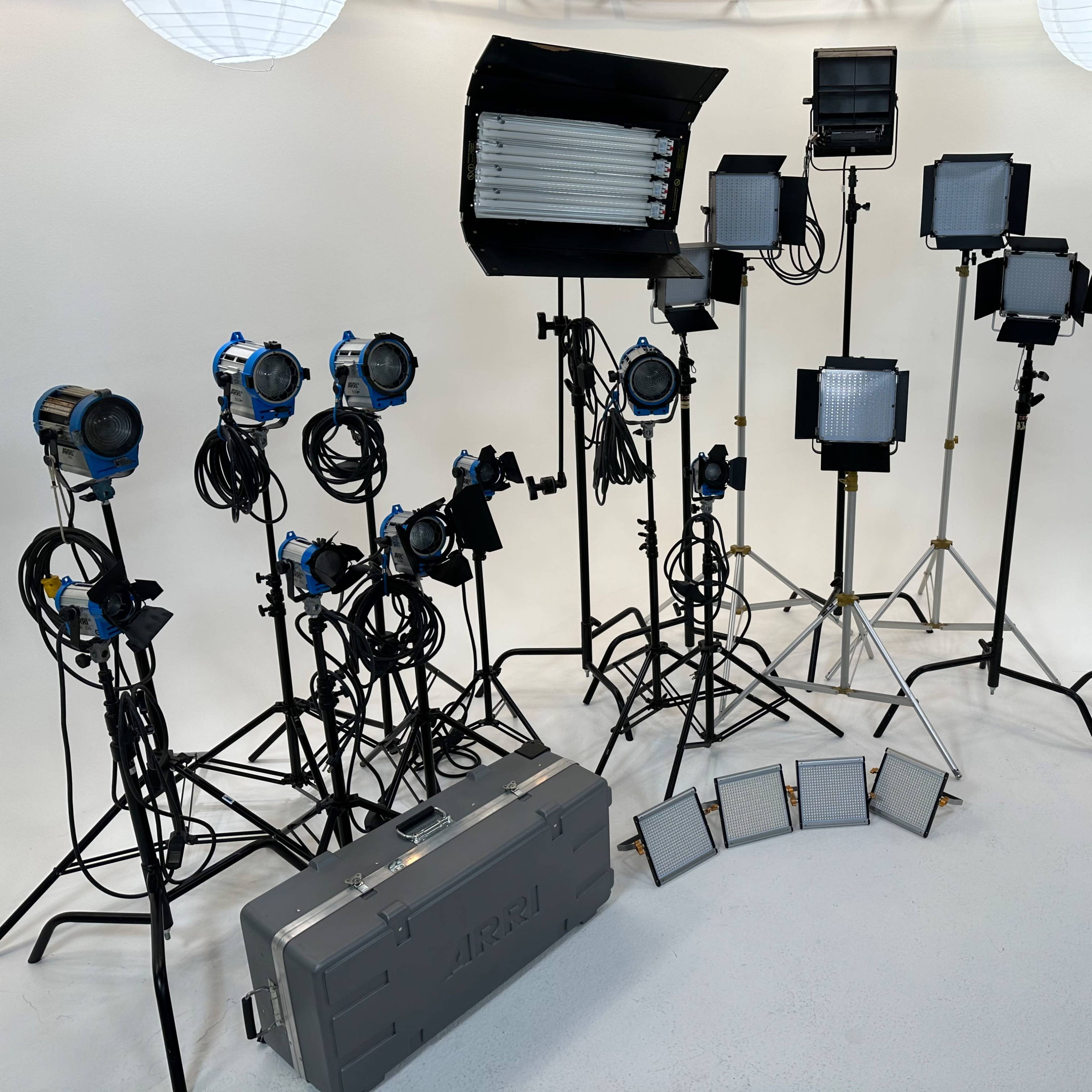 A collection of film lighting equipment arranged in a studio setting, including various light fixtures on stands and a case labeled "ARRI."