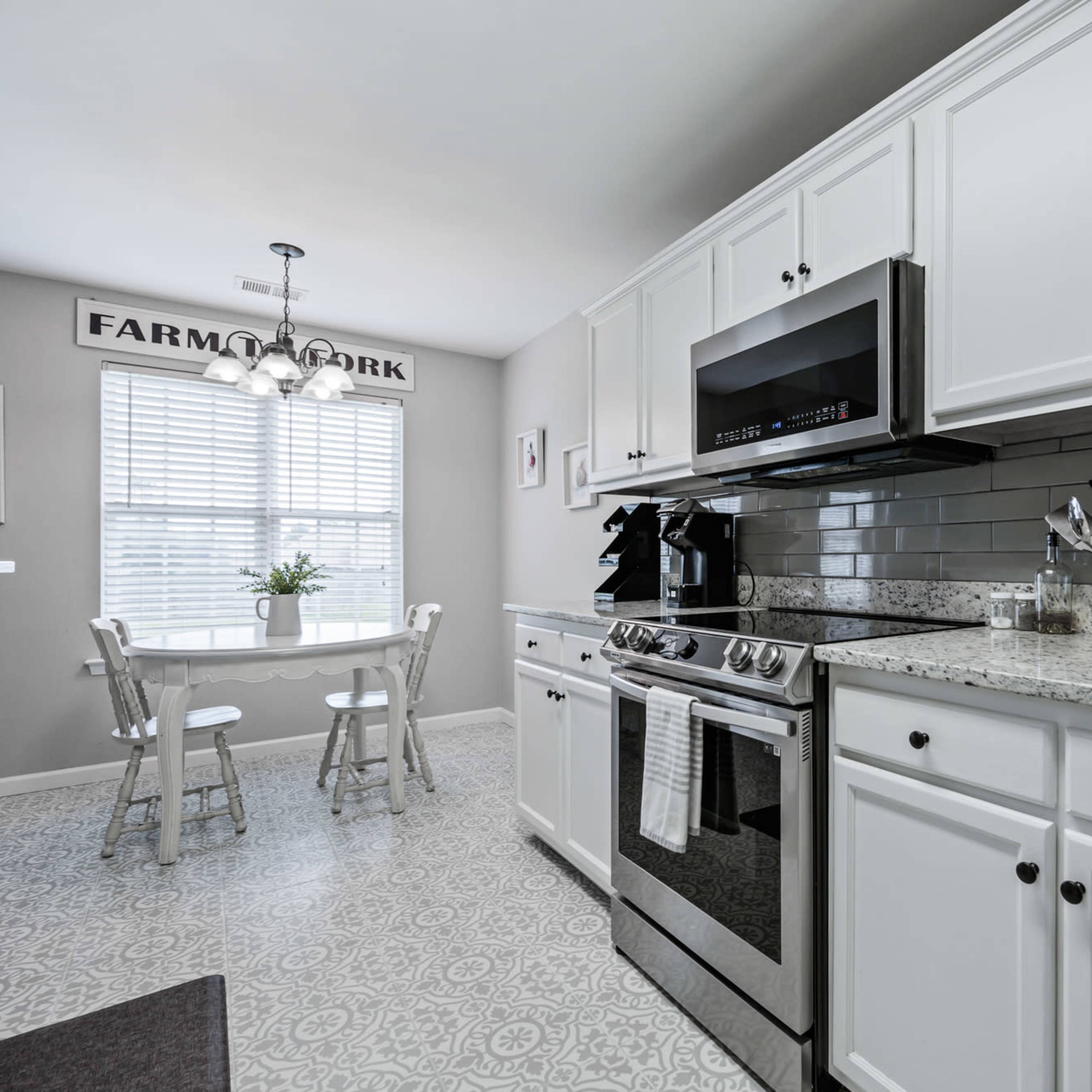 A modern kitchen features white cabinetry, stainless steel appliances, and a small dining table with chairs near a window.