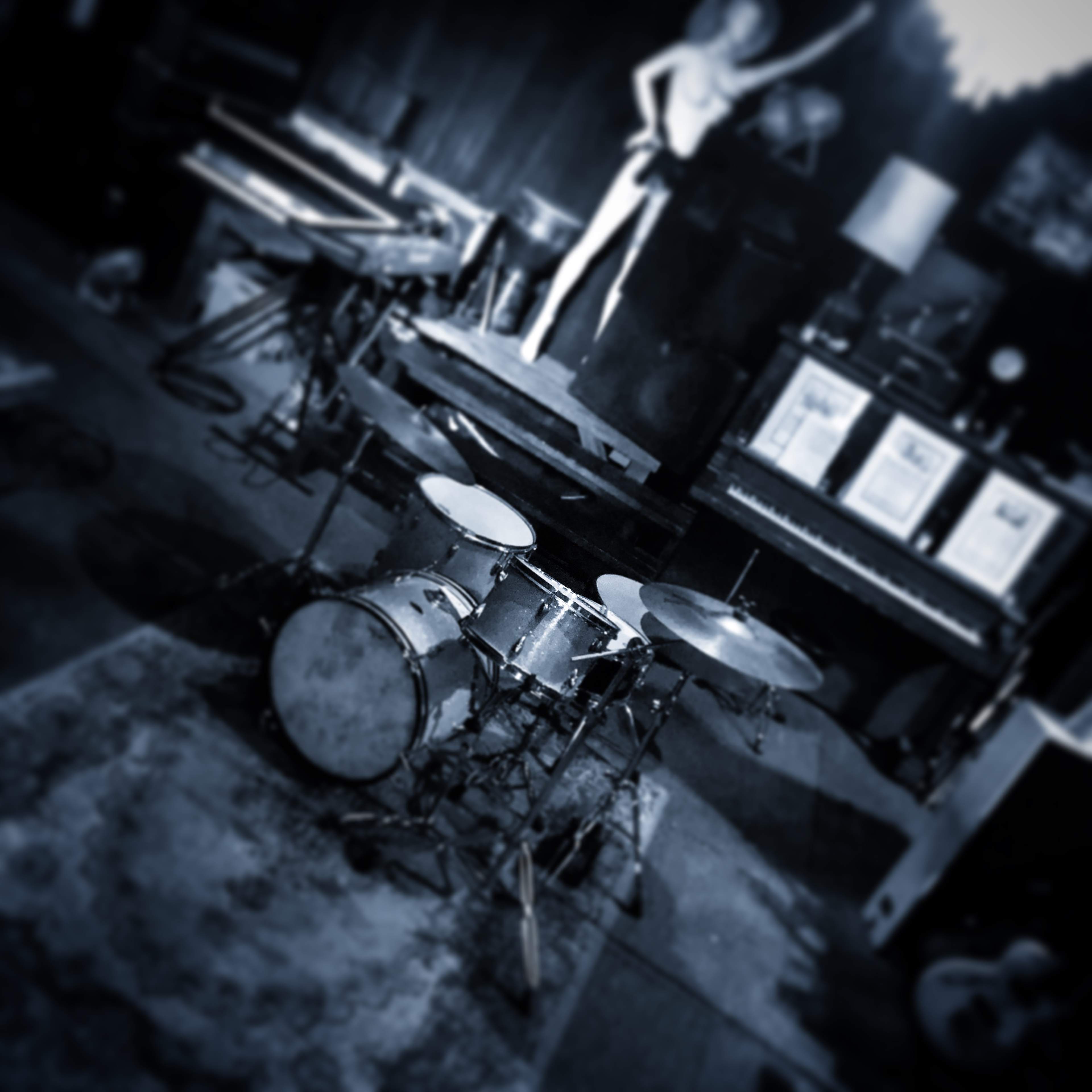 A drum set positioned on a carpet in a room filled with musical instruments and a decorative figure in the background.