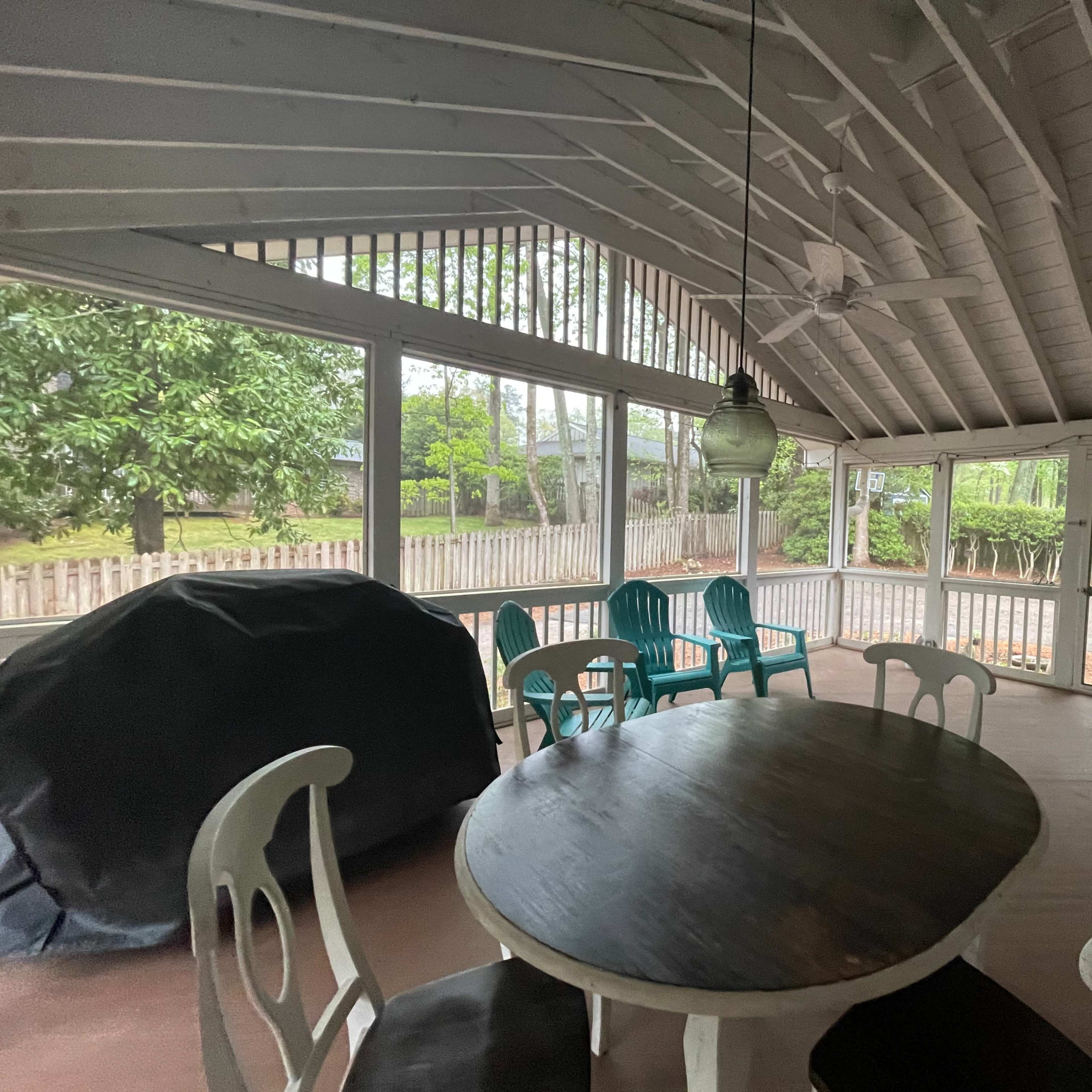 A screened-in porch with a round table and several light blue chairs, overlooking a garden area.