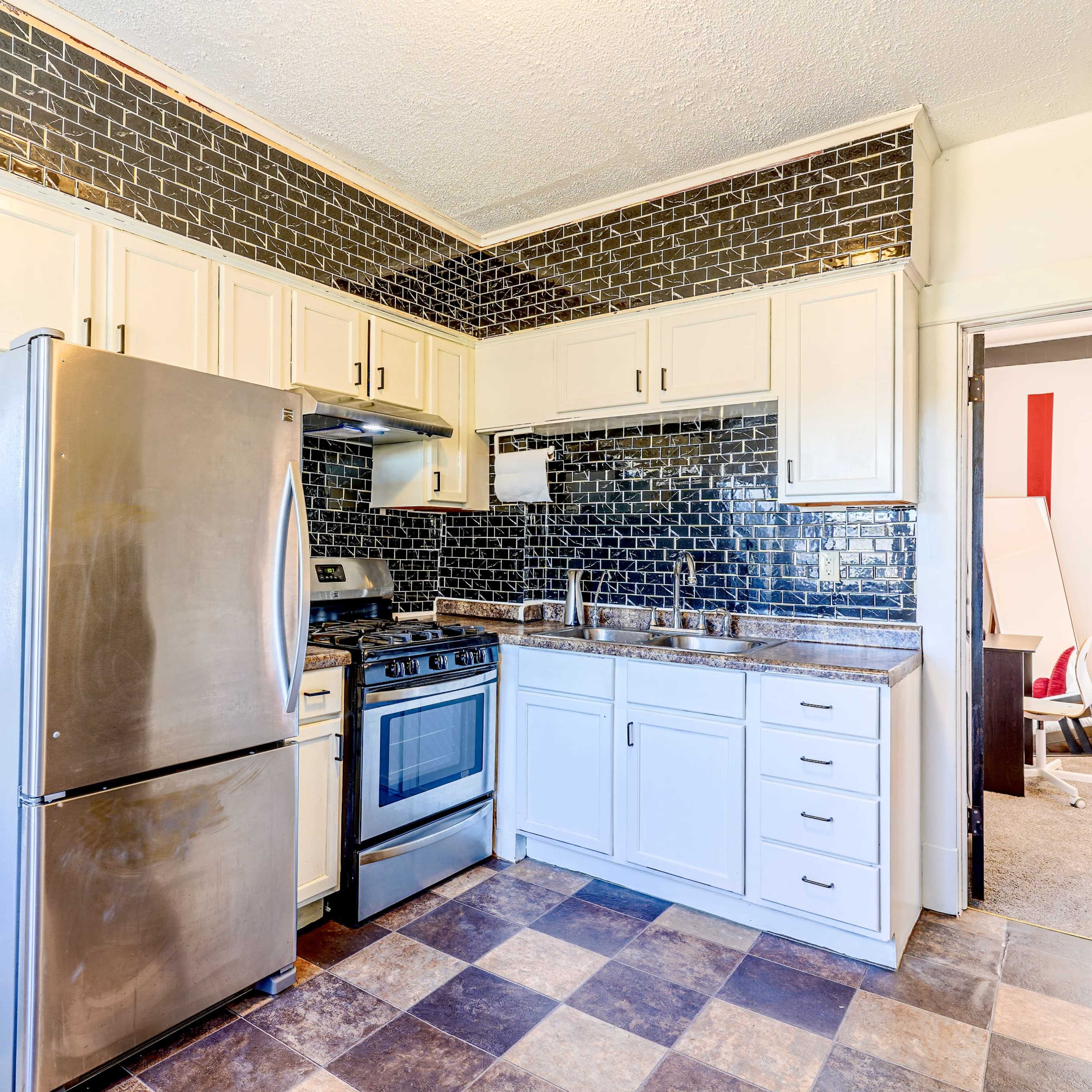 A compact kitchen featuring stainless steel appliances, a tile backsplash, and light-colored cabinetry.