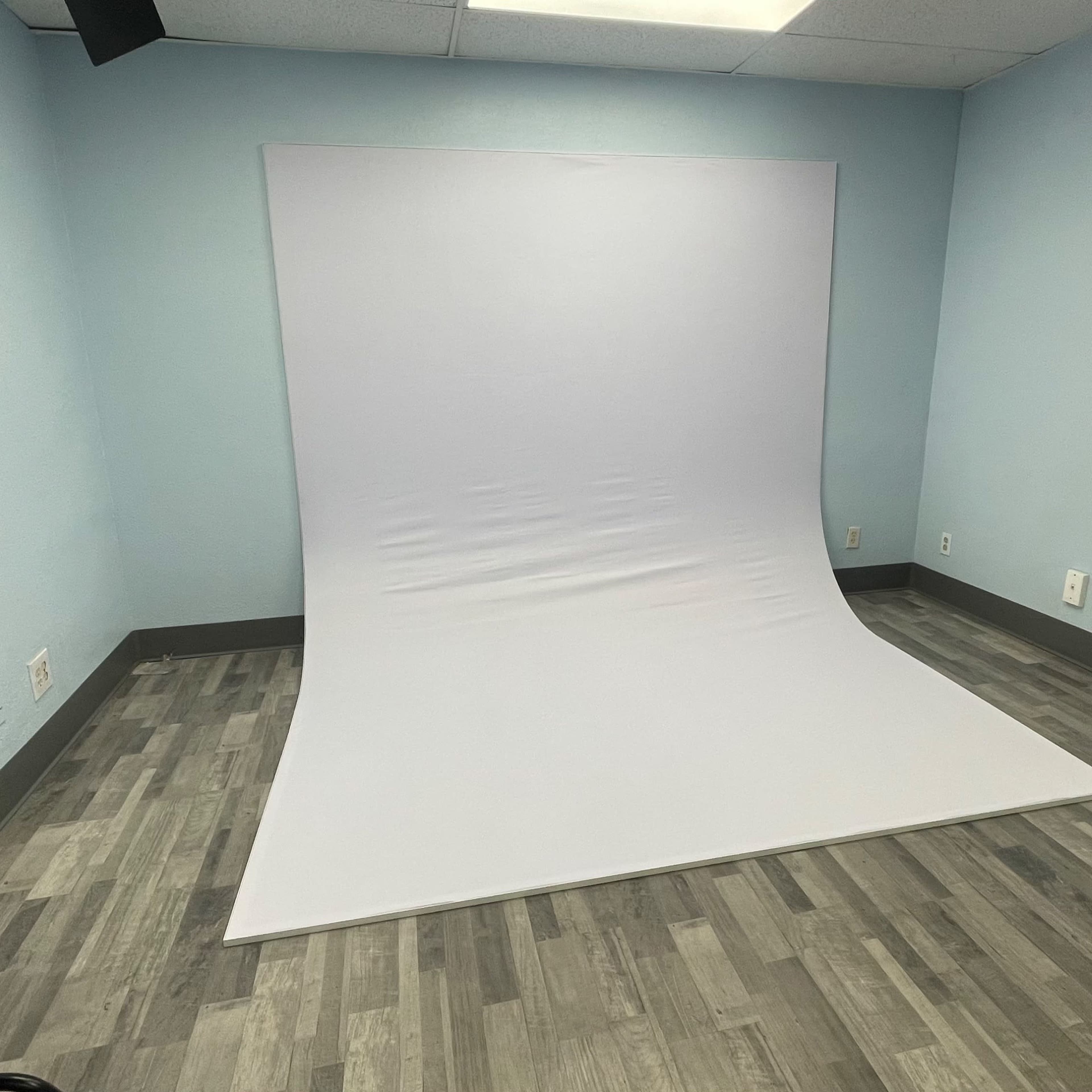 A blank photography studio with a white backdrop set against light blue walls and a wooden floor.