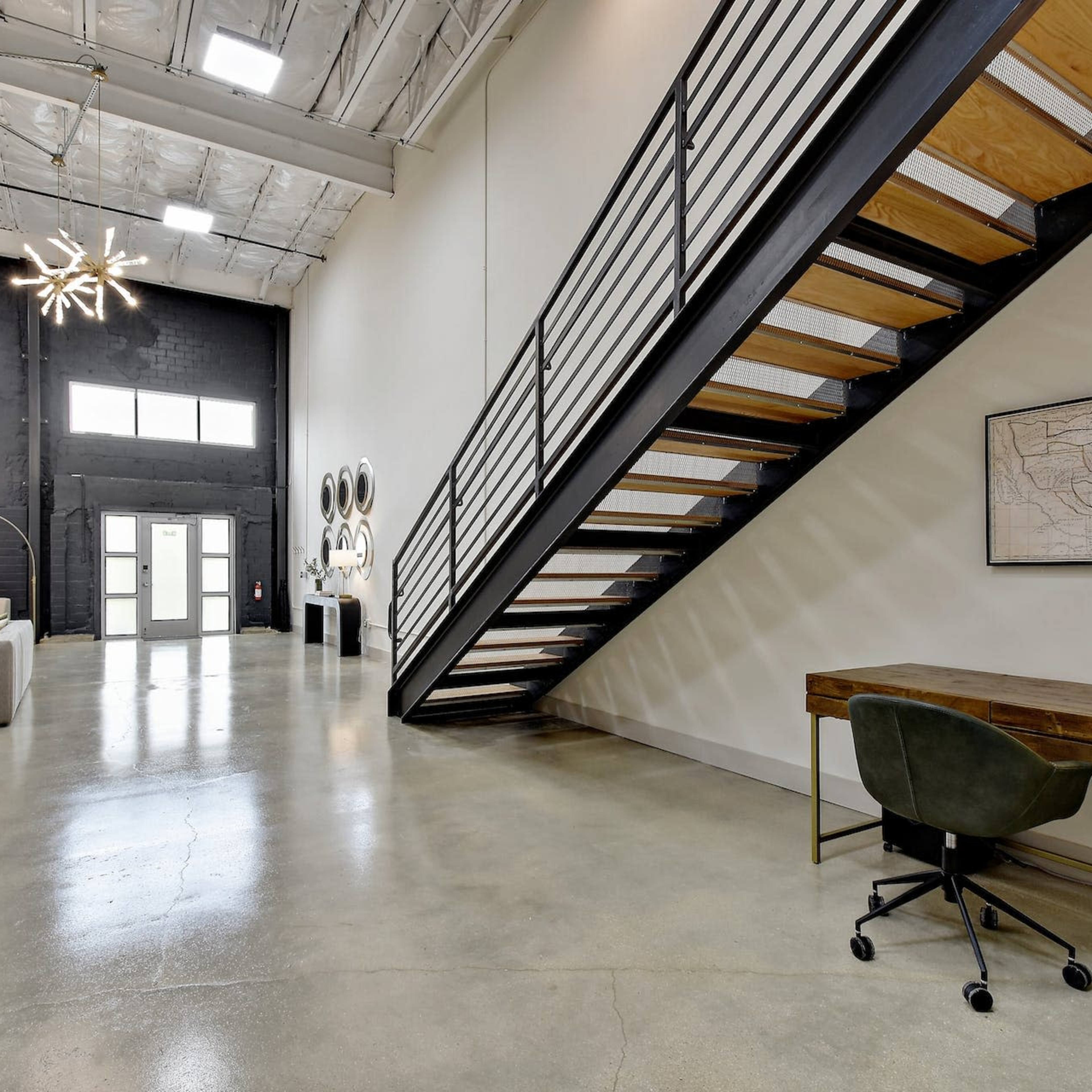 An industrial-style interior featuring a wooden staircase, a desk with a chair, and modern light fixtures.