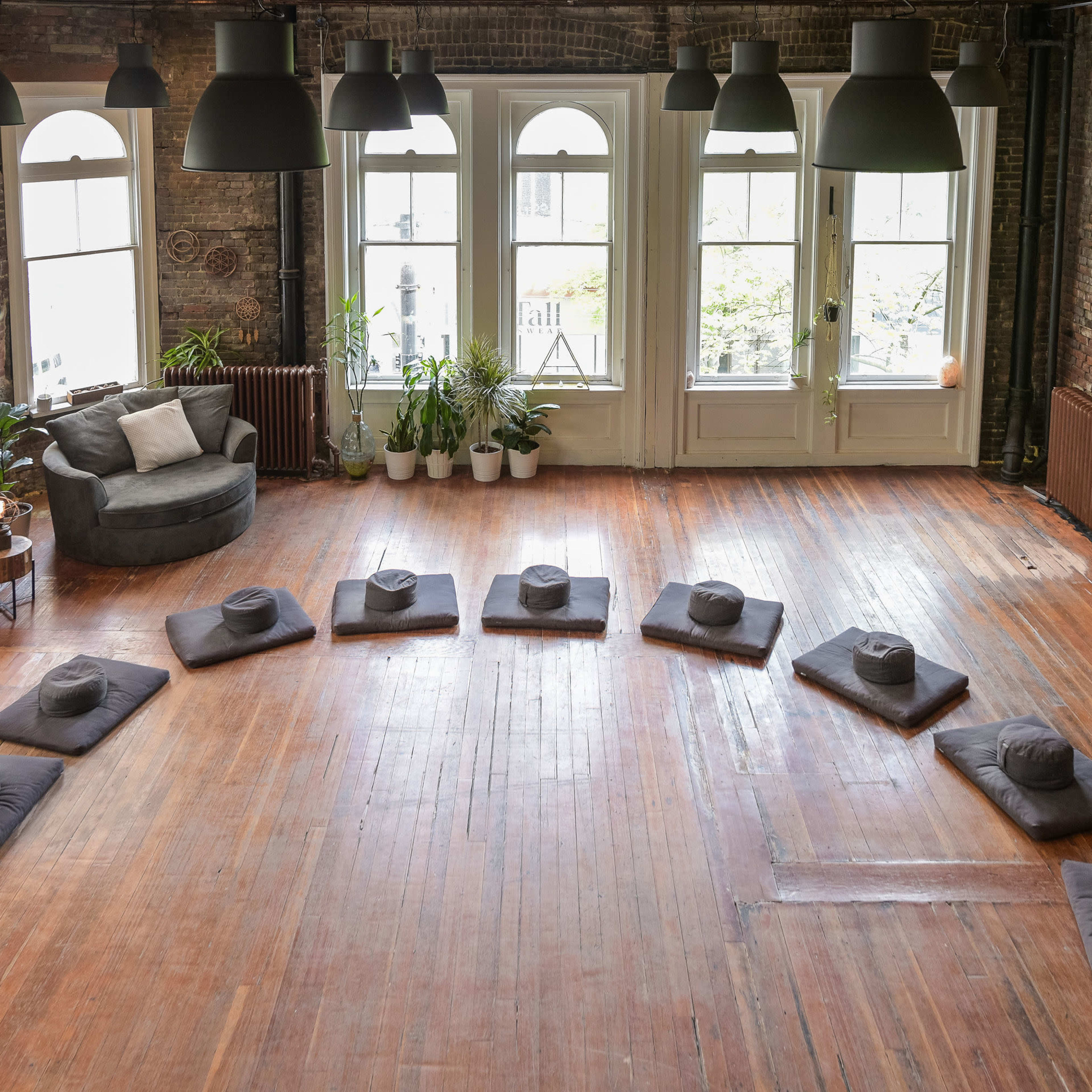 A spacious room with hardwood floors features a circular arrangement of cushions and a cozy seating area in the corner.