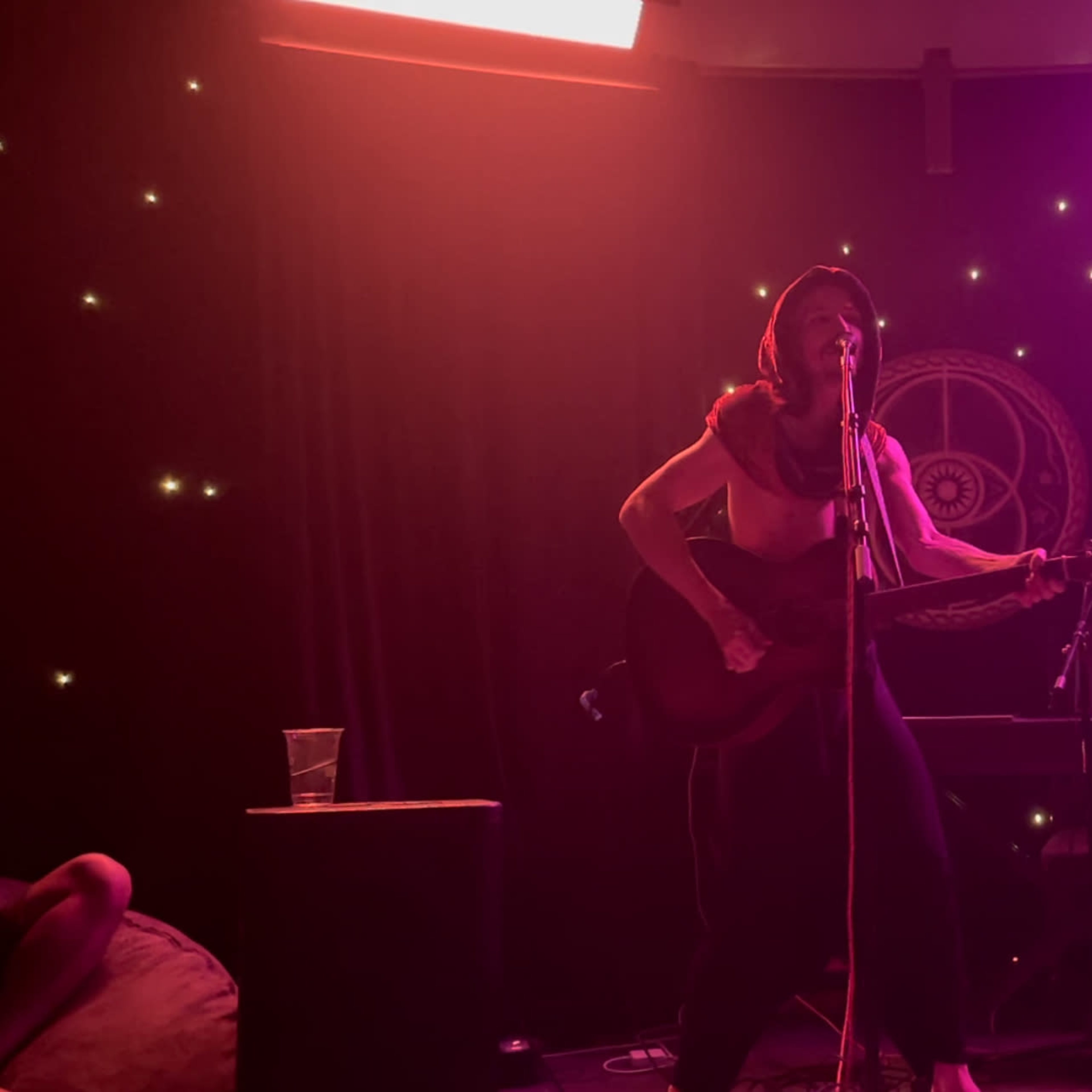A singer performs on stage with a guitar, in front of a backdrop adorned with lights.